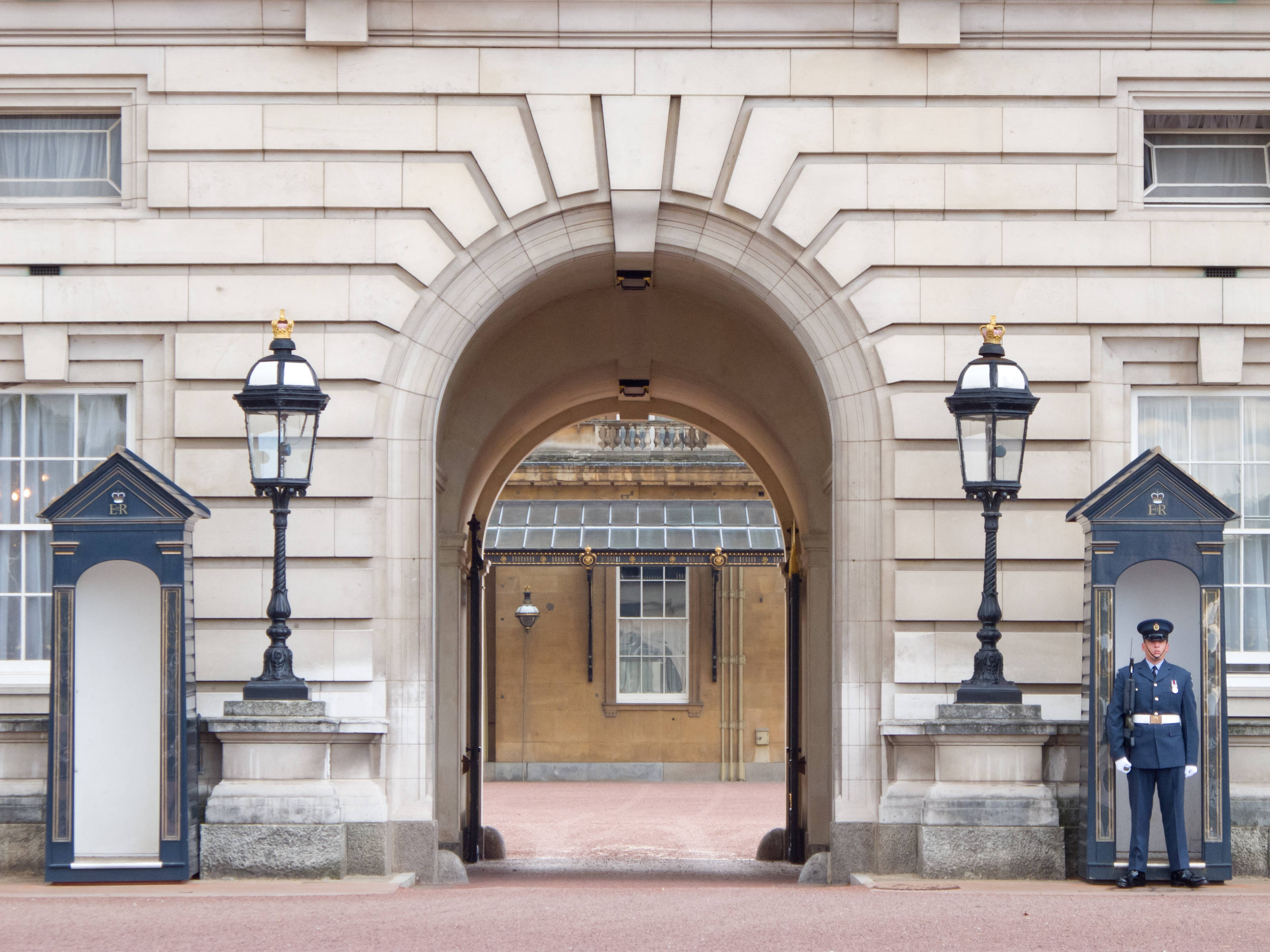 England 桌布 壁紙 — 一名皇家衛兵在一個宏偉的石拱門旁立正，拱門兩側有華麗的燈飾和崗亭。