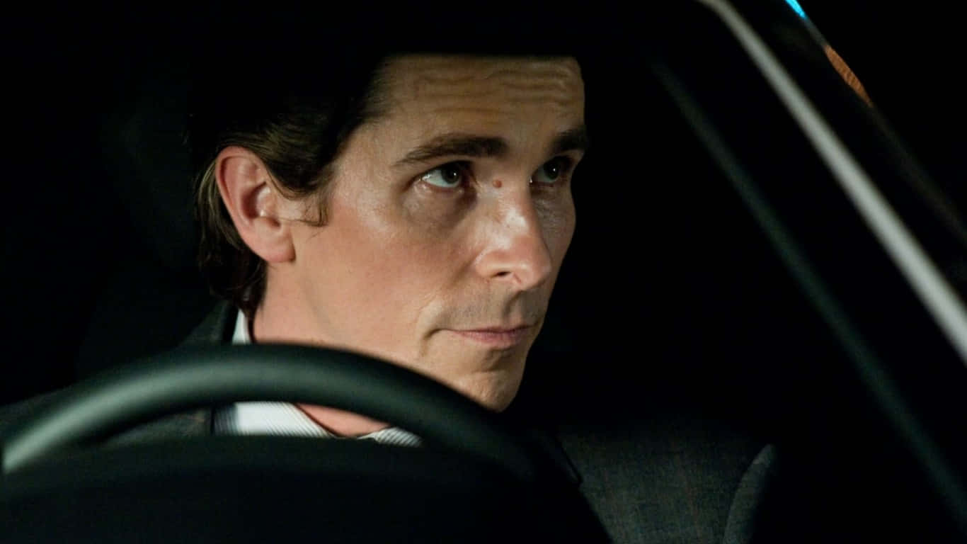 Bruce Wayne 桌布 壁紙 — 一名眼神銳利的男子在夜間從黑暗的車內向前凝視，被單一光源照亮。