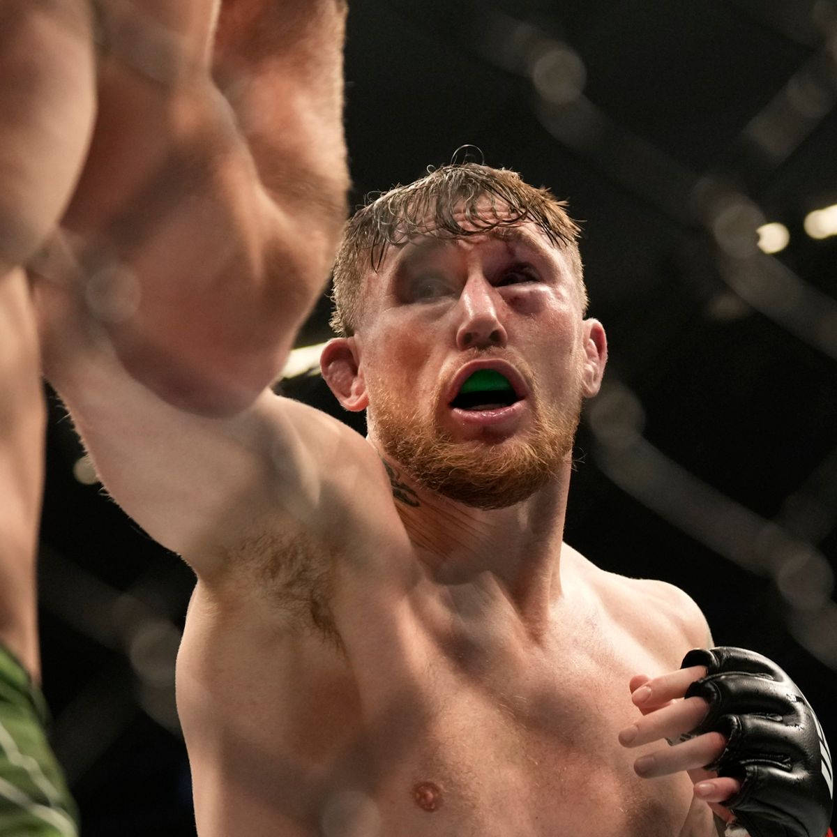 UFC 桌布 壁紙 — 一名眼部流血、戴著綠色護齒的拳手在激烈的MMA比賽中於籠內咆哮。