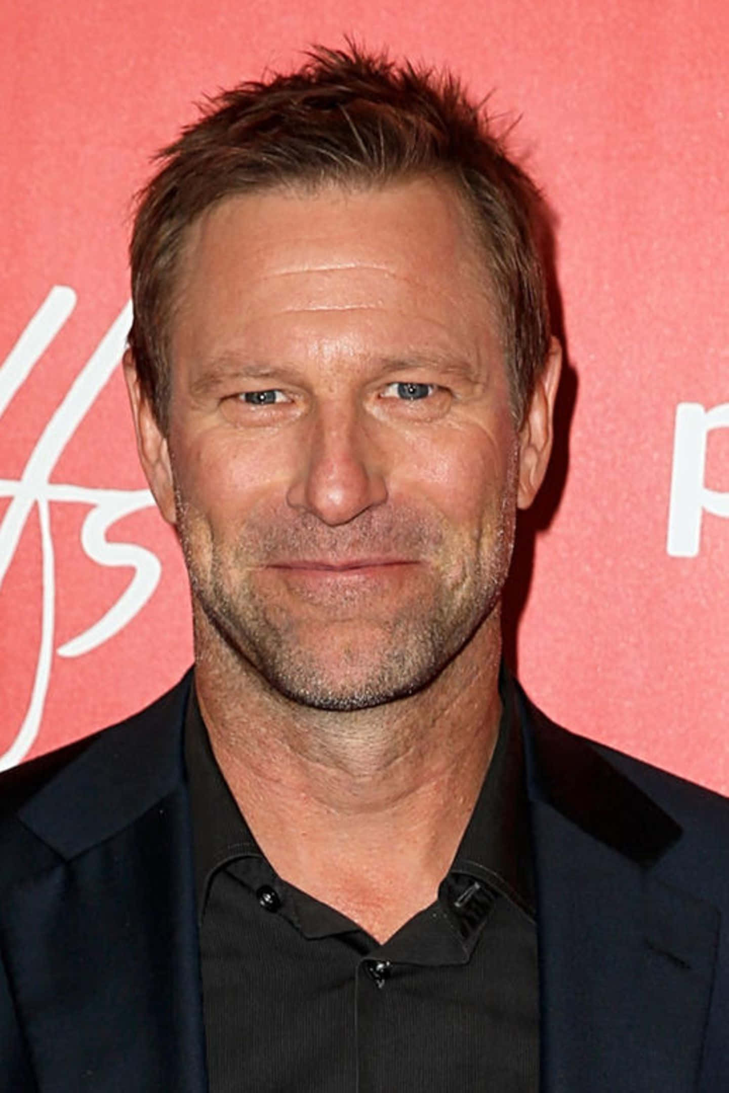Celebrity 桌布 壁紙 — 一名短棕髮、鬍渣男人的特寫肖像，身穿黑色西裝和襯衫，背景為粉紅色，帶有白色字樣。