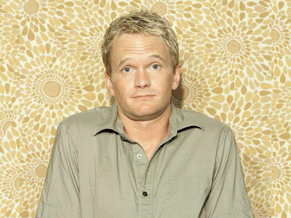 neil patrick harris 桌布 壁紙 — 一名短金髮、表情中性的男子站在一款米色和奶油色調、帶有太陽光線圖案的壁紙前。