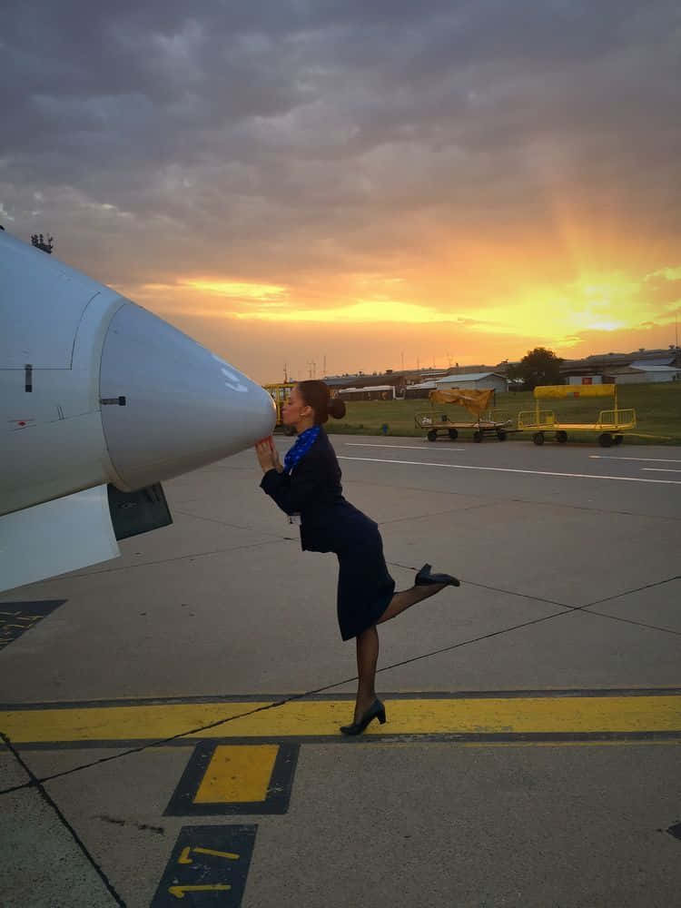 Aircraft 桌布 壁紙 — 一名空服員在充滿戲劇性雲彩的 vibrant 日落時分，在停機坪上親吻飛機的機頭。