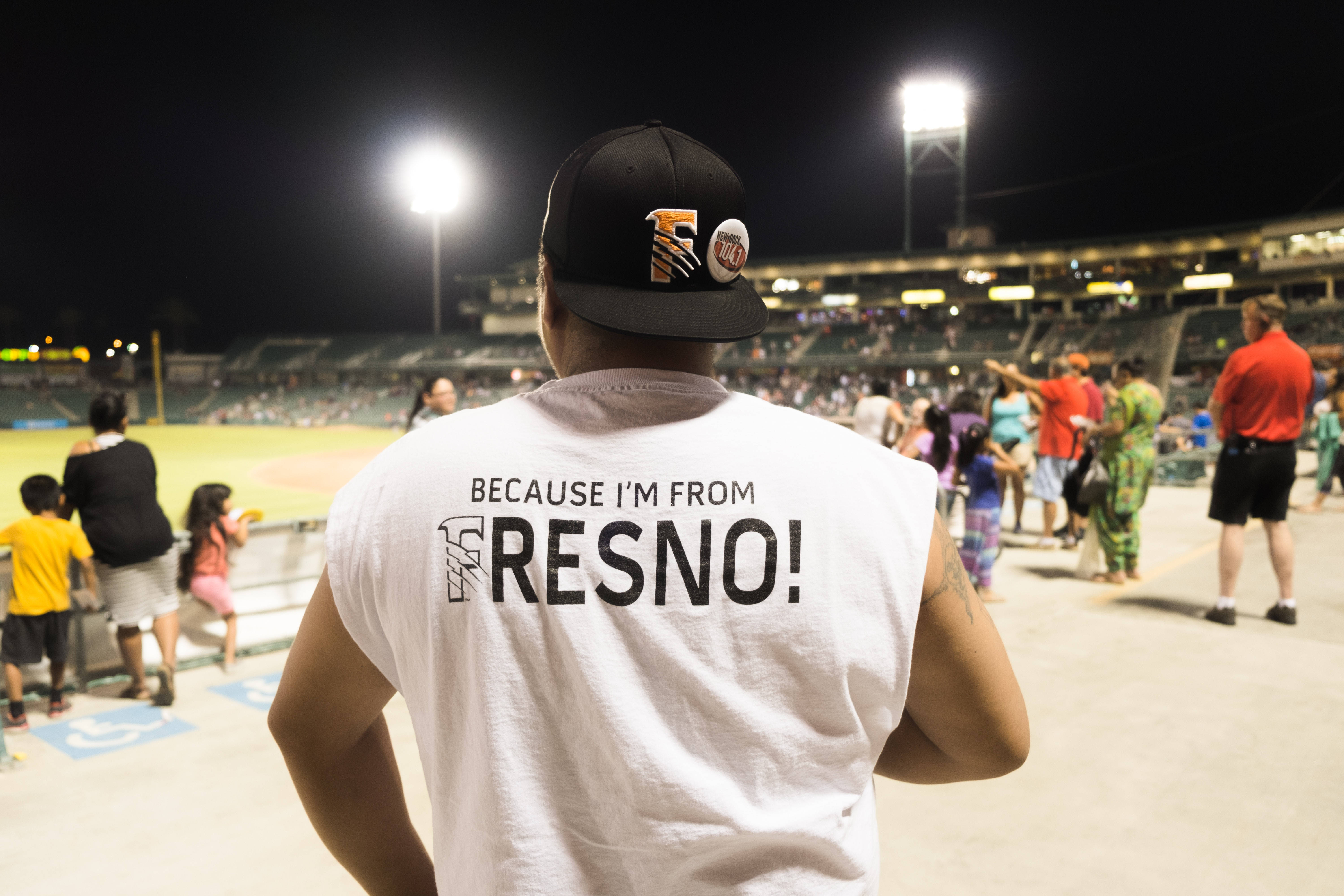 加州 桌布 壁紙 — 一名穿著 Fresno 驕傲背心的男子在夜間棒球場上，在明亮的泛光燈下觀看比賽。