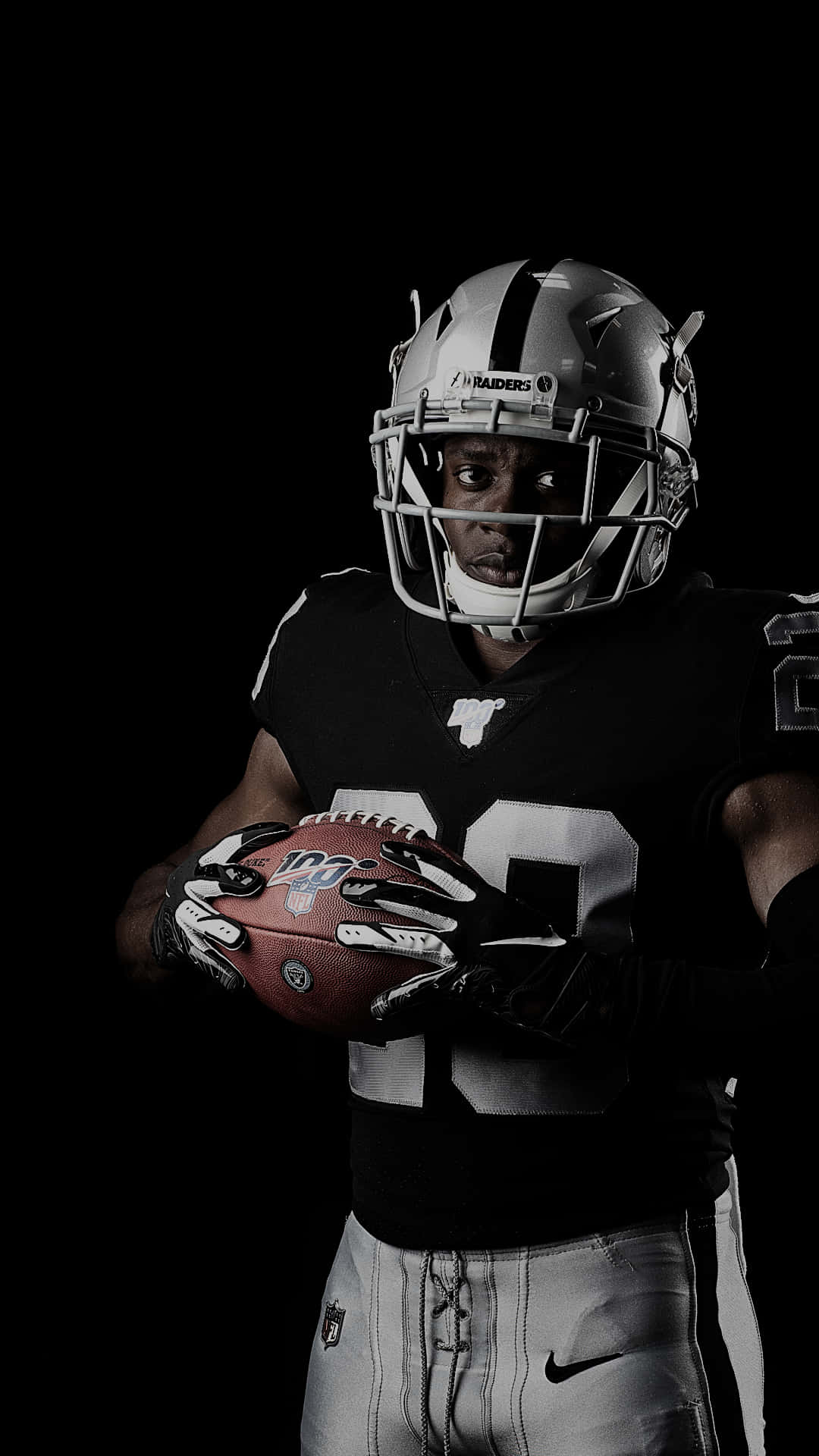 穿著Raiders裝備的足球運動員在黑暗的攝影棚中持球。 — 突襲者 GIF 壁紙