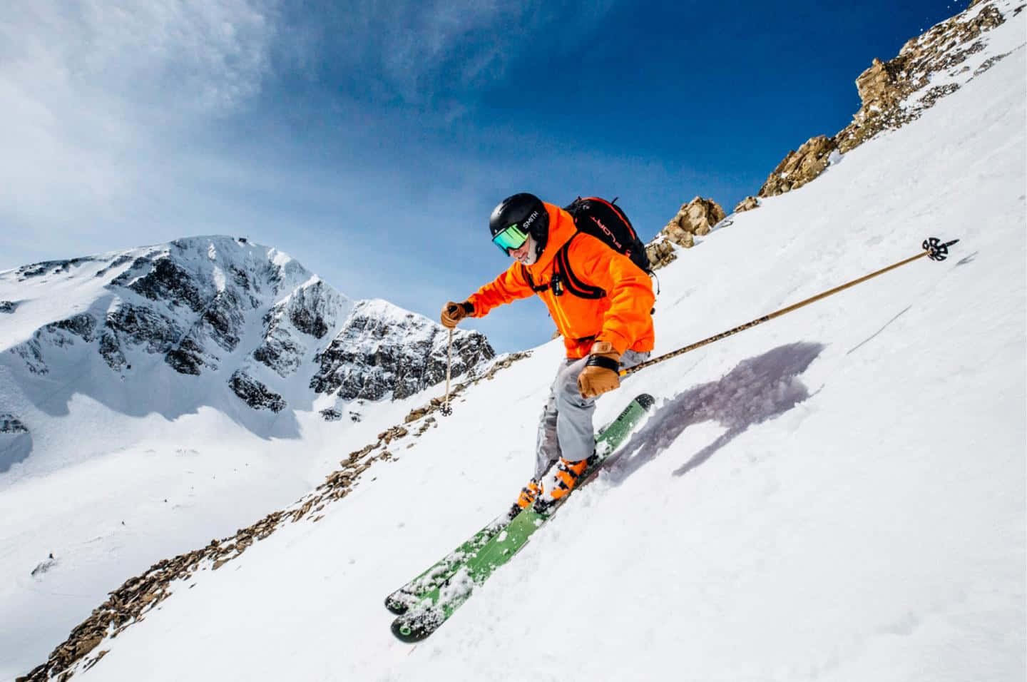 ski 桌布 壁紙 — 一名穿著亮橙色外套的滑雪者，在晴朗的藍天下沿著白雪皚皚的山坡滑下。