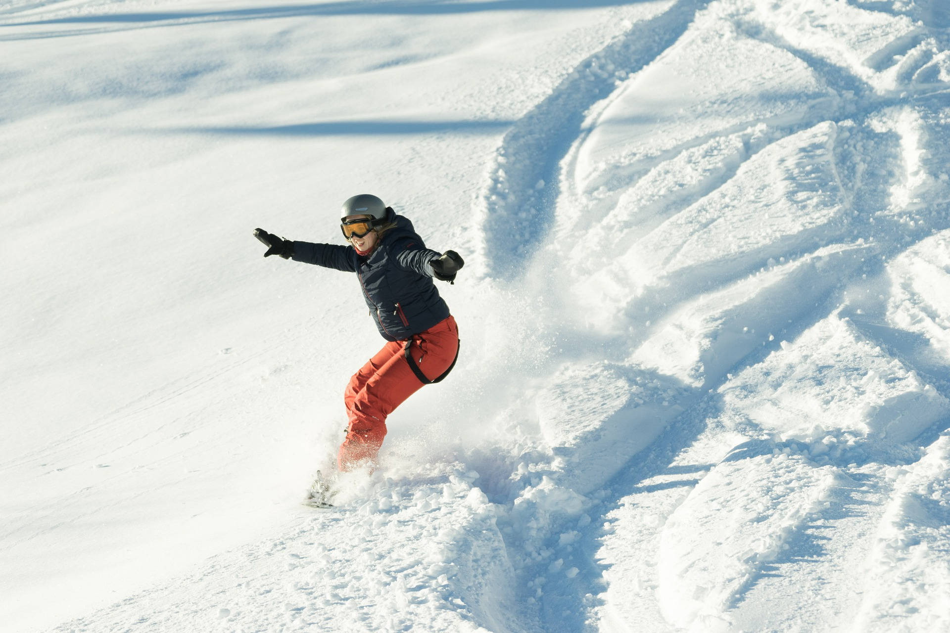 Snowboarding 桌布 壁紙 — 一名穿著亮橙色褲子的滑雪板運動員在陽光明媚的山坡上穿過新鮮的粉雪。
