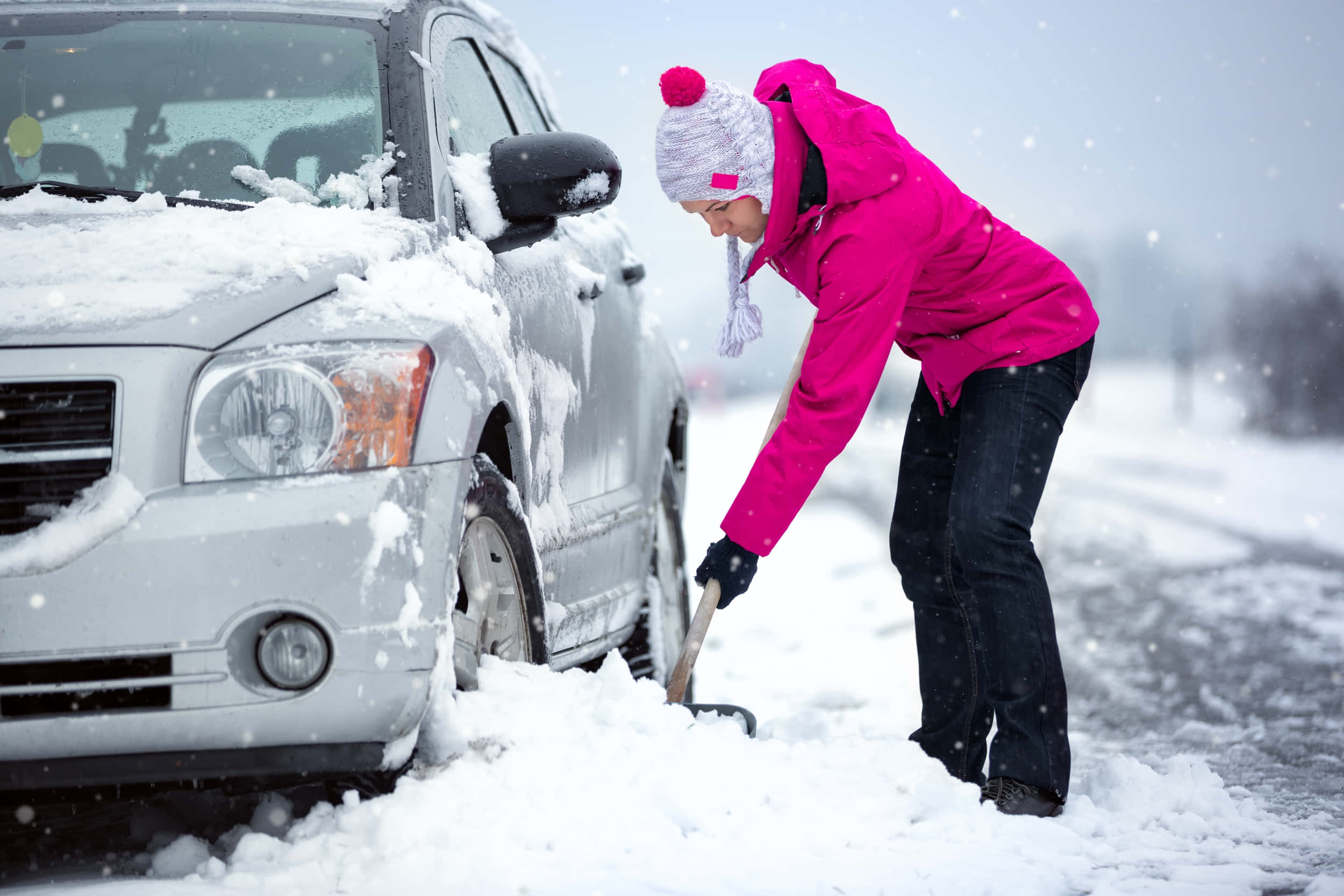 Winter Driving 桌布 壁紙 — 一名穿著亮粉色外套的人在下雪的冬日將銀色汽車上的雪鏟走。