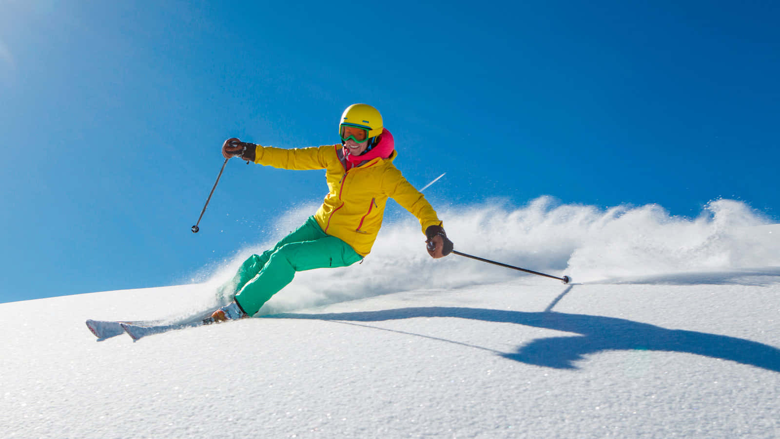 ski 桌布 壁紙 — 一名穿著亮黃色外套和綠色褲子的滑雪者在晴朗的藍天下穿過新鮮的粉雪。