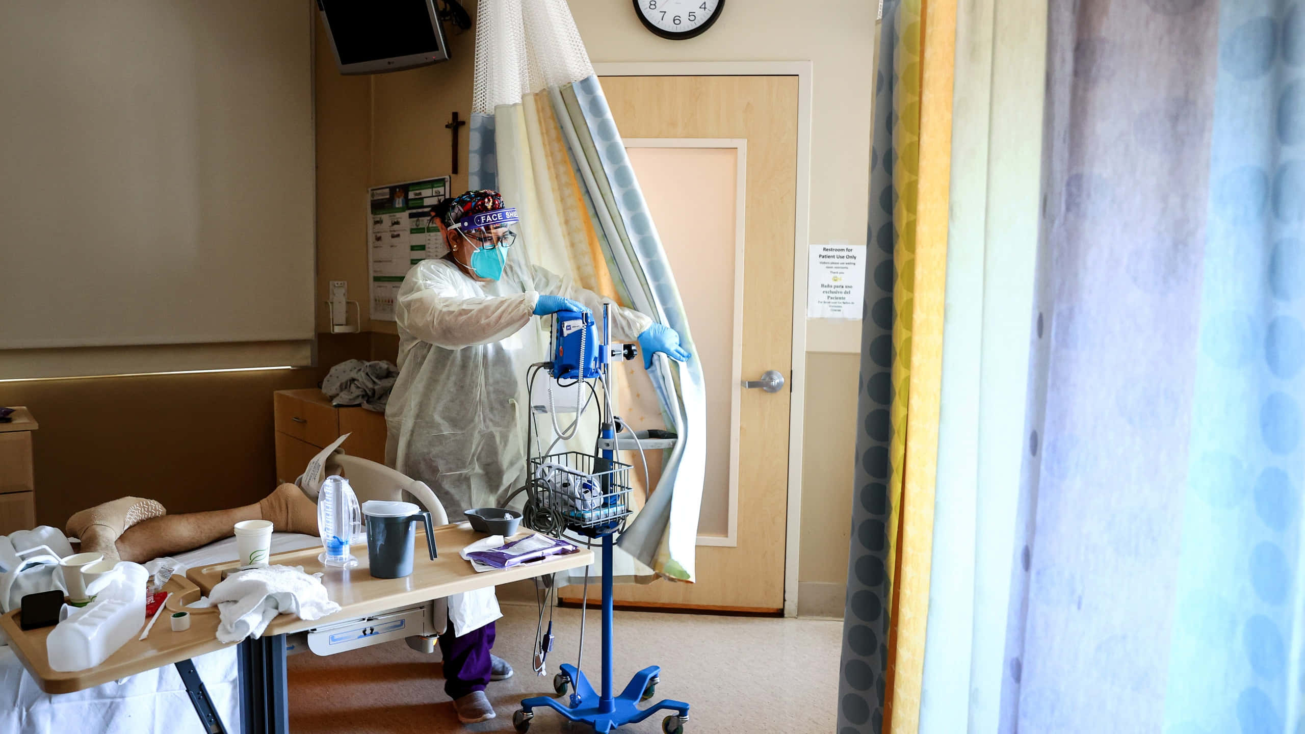 Hospital 桌布 壁紙 — 一名穿著全套防護裝備的醫護人員正在調整病房內的窗簾，病房床上有一名病人。