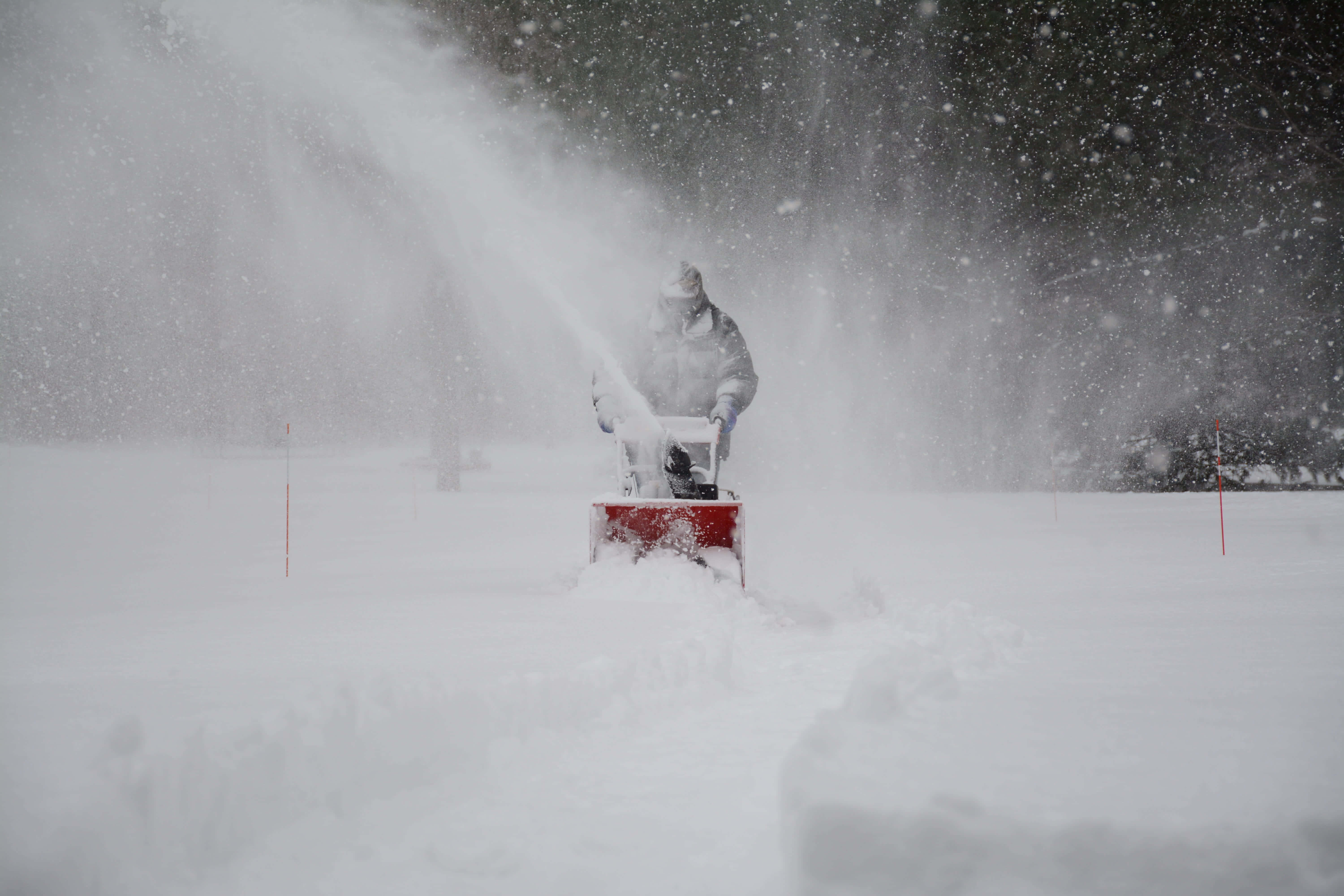 Snowplow 桌布 壁紙 — 一名穿著冬季裝備的人正在操作一部紅色吹雪機，在暴風雪中噴出積雪，周圍雪花飄落。