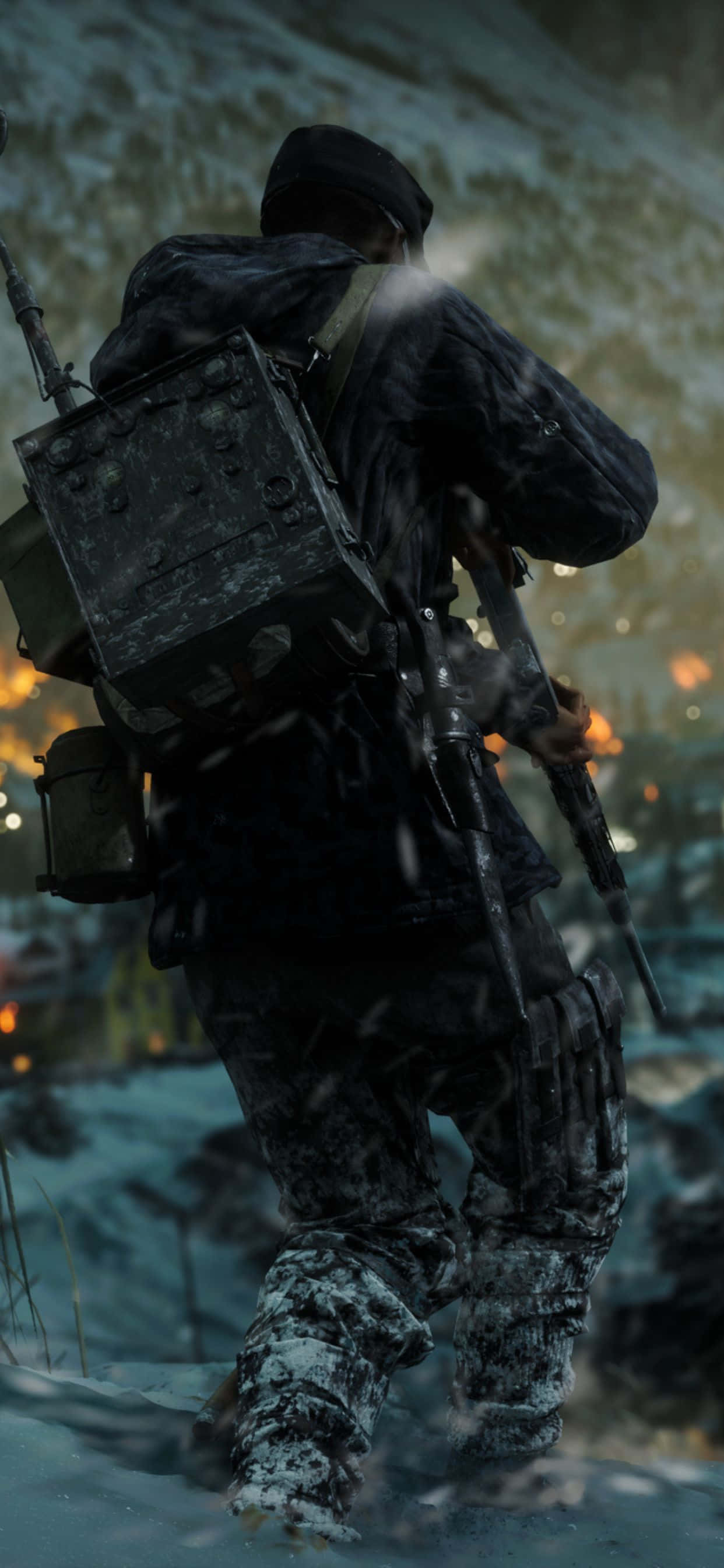 HD Battlefield V 桌布 壁紙 — 一名穿著冬季裝備的士兵帶著步槍和裝備走過雪地，背景中遠處的火光閃爍。