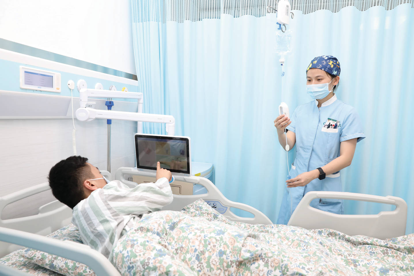 Nurse 桌布 壁紙 — 一名穿著制服和口罩的護士正在檢查靜脈注射，而病床上的病人正在使用平板電腦。