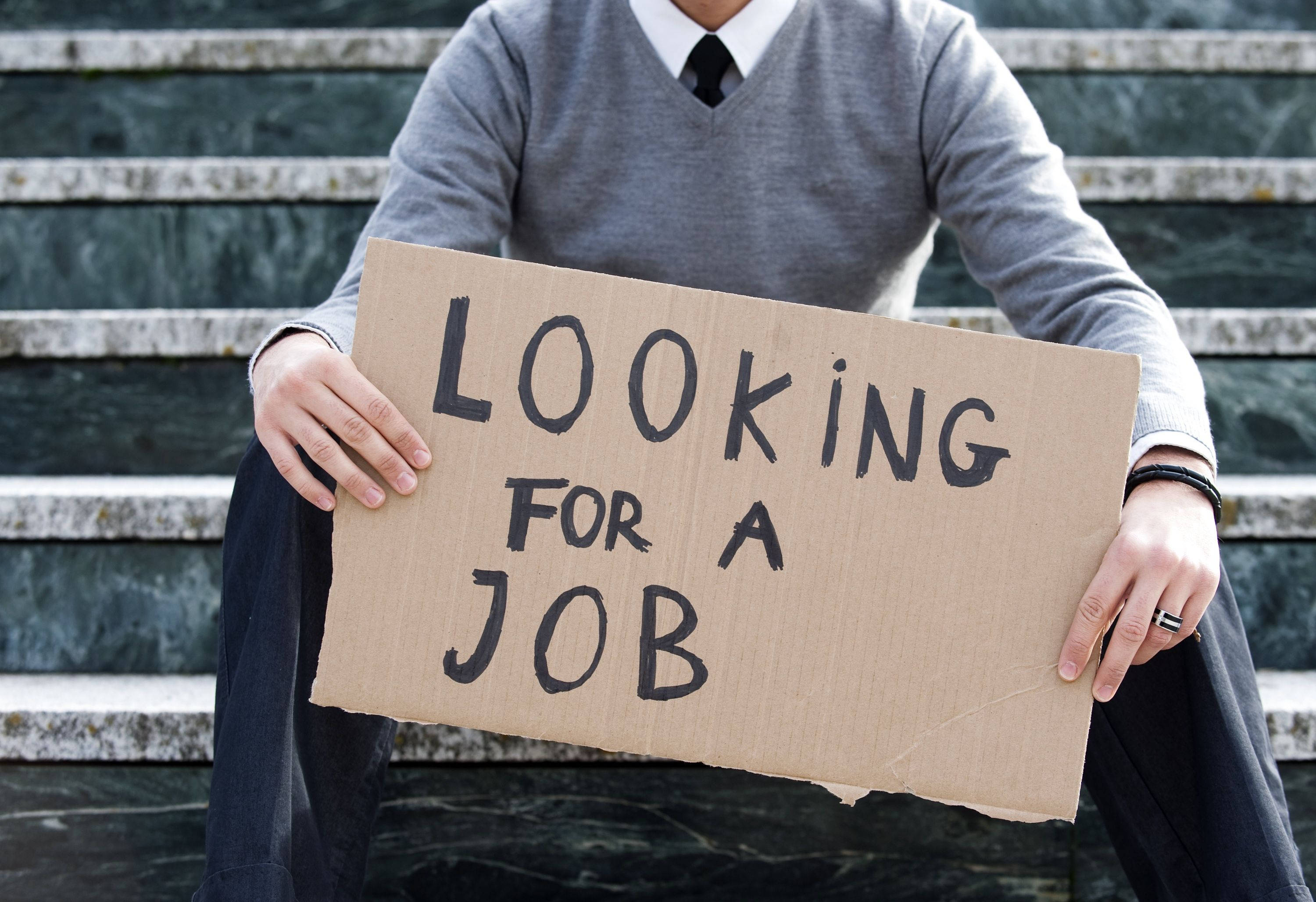 Typography 桌布 壁紙 — 一名穿著商務服裝的人坐在石階上，舉著一個寫著 looking for a job 的紙板標語。