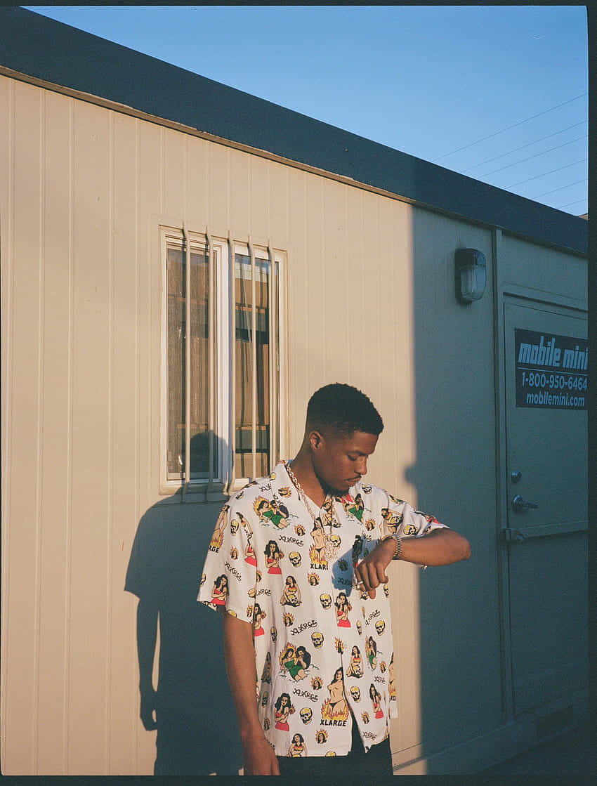 Pierre Bourne 桌布 壁紙 — 一名穿著圖案印花襯衫的年輕男子在金色陽光下，於移動式儲物櫃旁查看手錶。