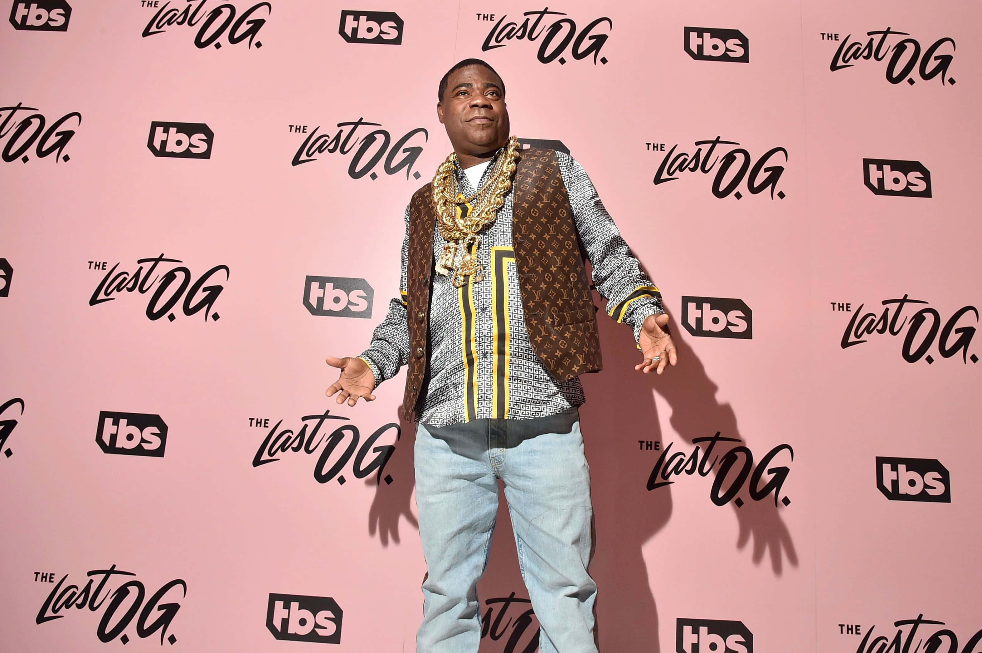Tracy Morgan 桌布 壁紙 — 一名穿著圖案背心和金鏈的男子在粉紅色背景前自信地擺姿勢，背景重複出現 'The Last O.G.' 和 'tbs' 標誌。