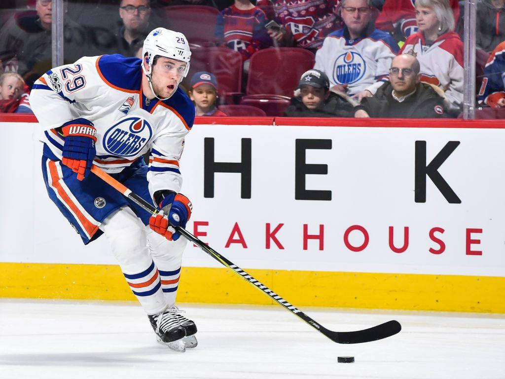 運動 桌布 壁紙 — 一名穿著埃德蒙頓油人隊裝備的曲棍球球員在冰上激烈滑行，帶著冰球，前方有歡呼的球迷。