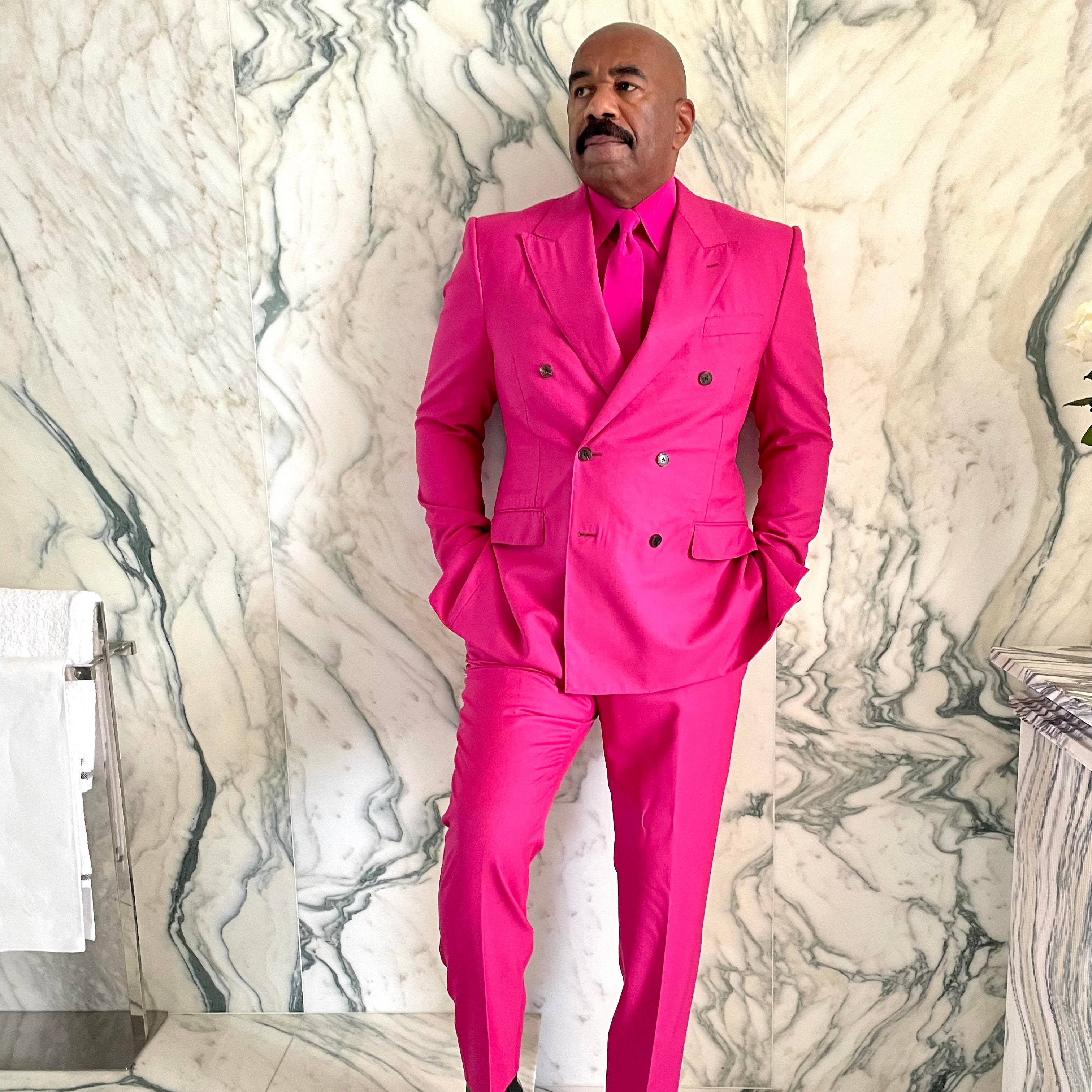 steve harvey 桌布 壁紙 — 一名穿著大膽粉紅色雙排扣西裝的男子，自信地站在豪華浴室中白色和綠色大理石牆前。