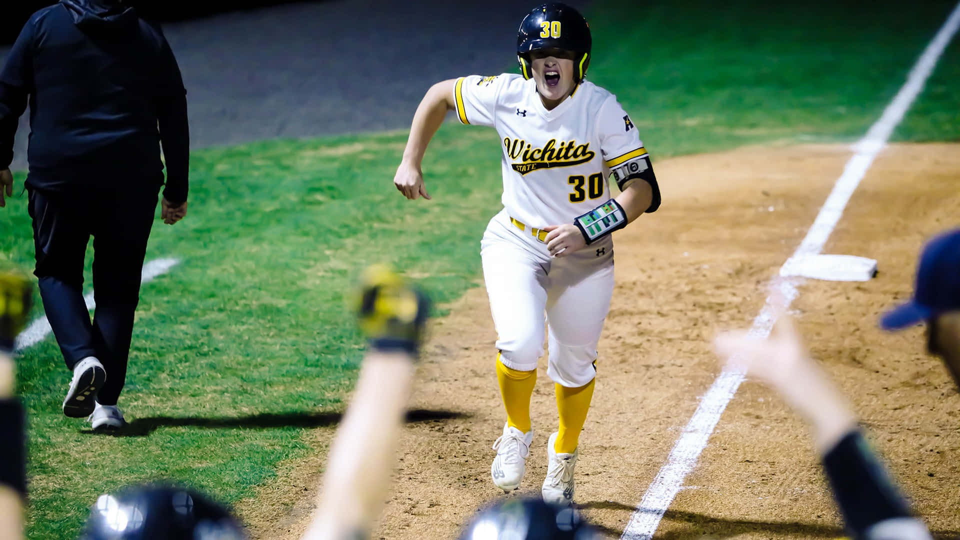 Little League Baseball 桌布 壁紙 — 一名穿著威奇塔州立大學球衣的棒球選手，在球場燈光下揮動手臂、張開嘴巴，勝利地衝向本壘板。