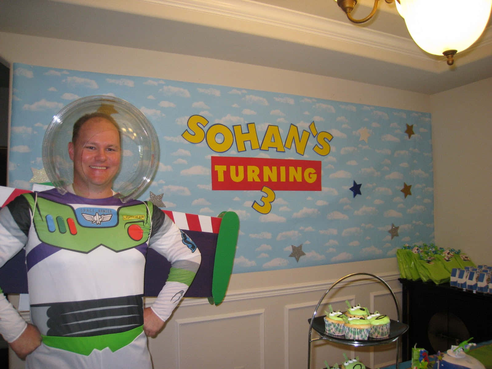 Toy Story Cloud 桌布 壁紙 — 一名穿著巴斯光年服裝的男子在藍天主題的生日背景前微笑，背景上有星星和「Sohan's Turning 3」文字。
