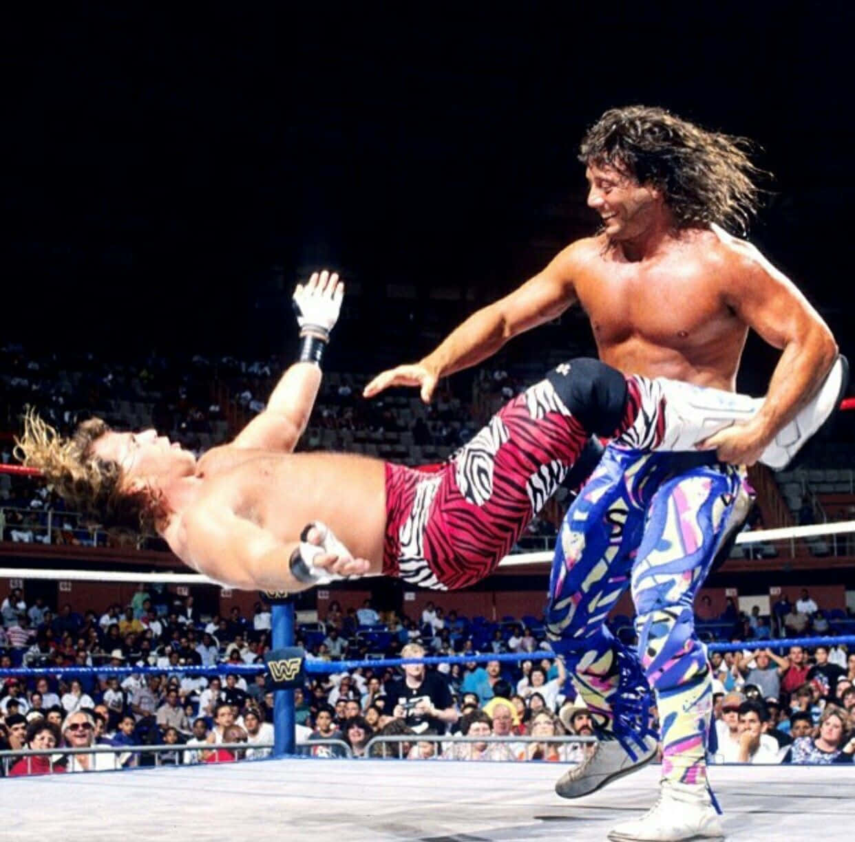 shawn michaels 桌布 壁紙 — 一名穿著彩色褲子的摔角手在擠滿觀眾的場館中將對手舉到空中，做出一個戲劇性的動作。