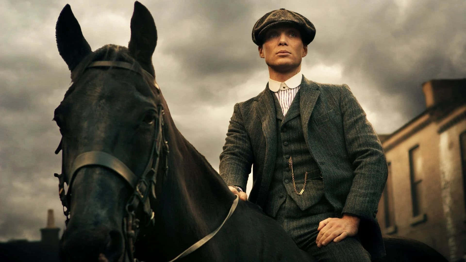 穿著復古西裝的男子在陰天騎著黑馬，附近有磚砌建築。 — Peaky Blinders 壁紙