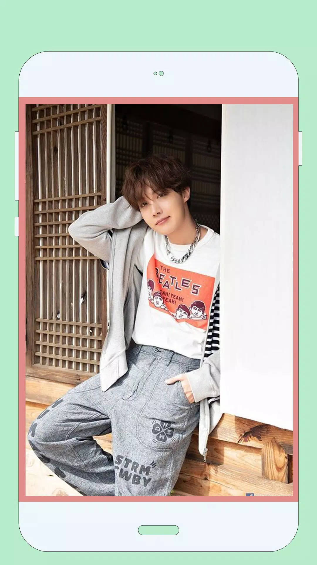 jhope 桌布 壁紙 — 一名穿著披頭四T恤和灰色運動褲的年輕男子，在智慧型手機螢幕上靠著木製格子門隨意擺姿勢。