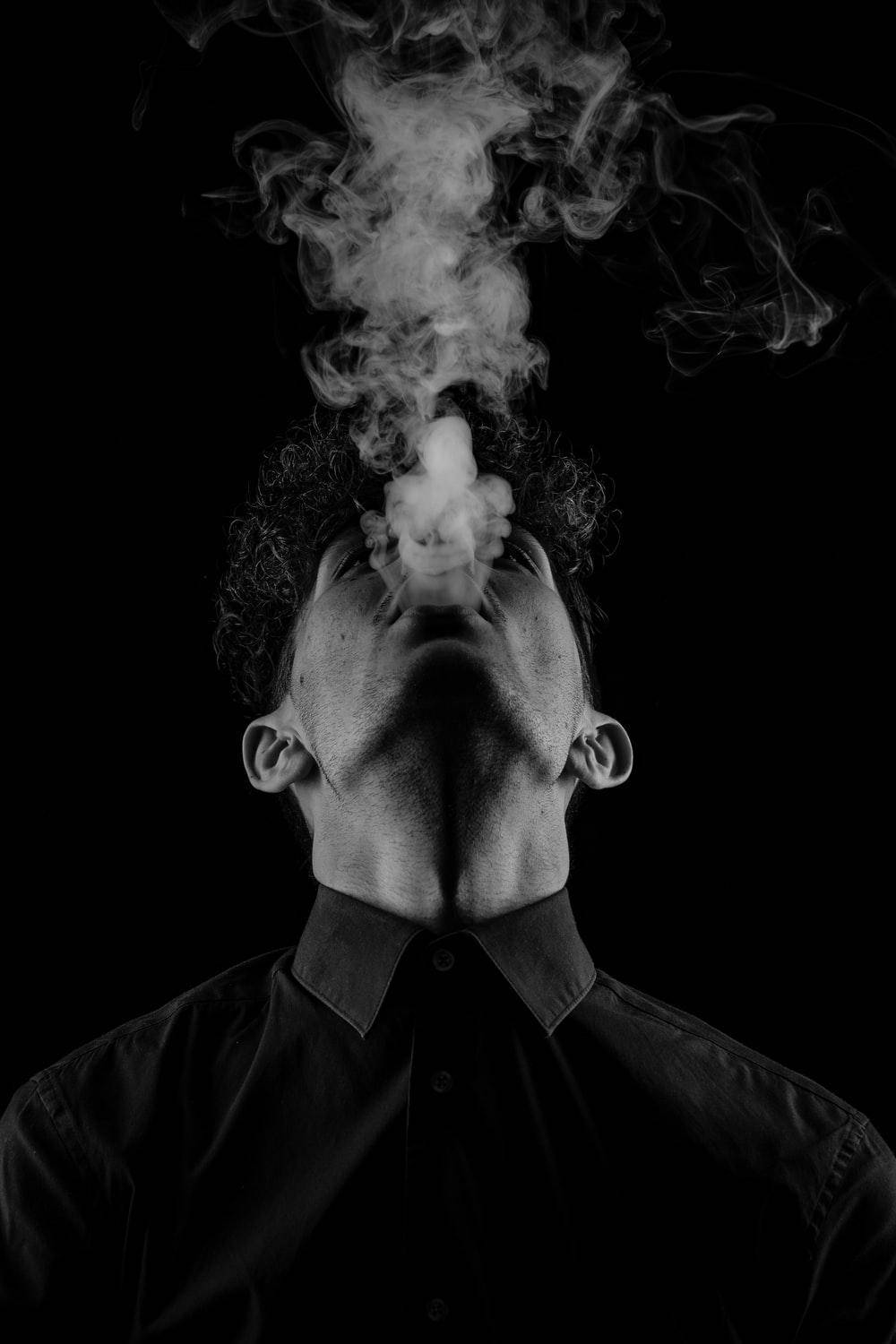 黑白 桌布 壁紙 — 一名穿著有領襯衫的男子，在強烈的黑色背景下，於戲劇性的黑白肖像中向上呼出濃煙。