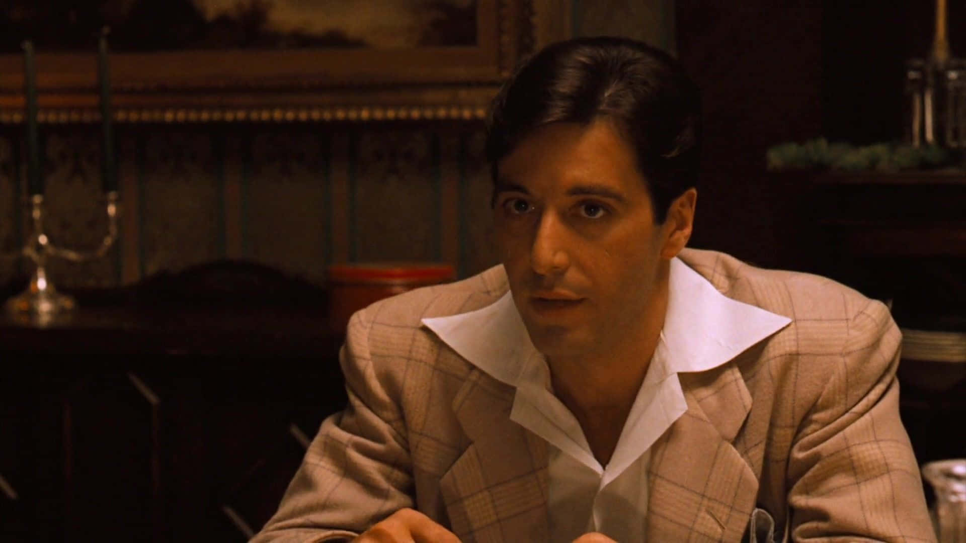 The Godfather 桌布 壁紙 — 一名穿著格子西裝的男子坐在光線昏暗、裝飾華麗且點著蠟燭的房間裡。