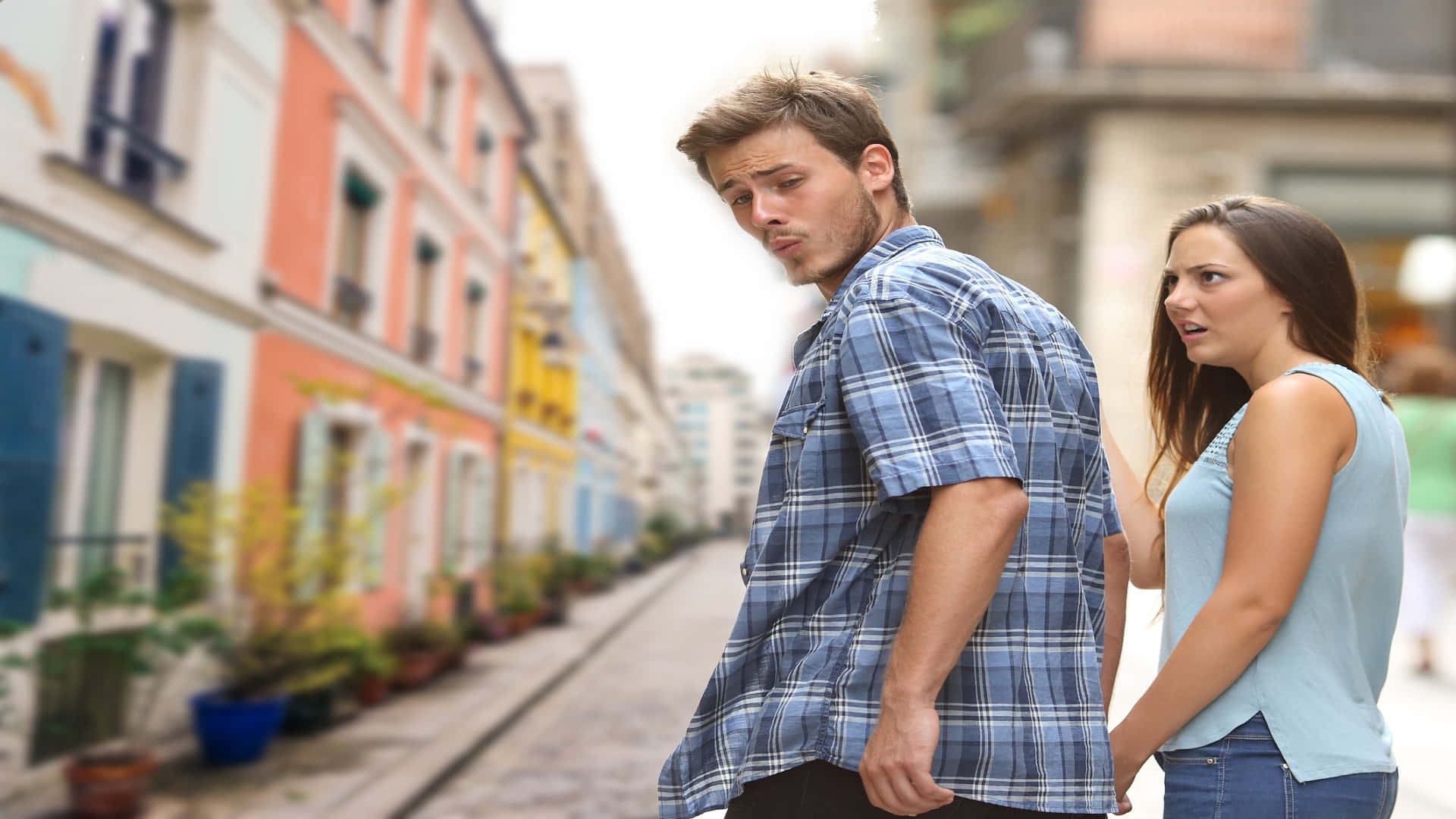 meme 桌布 壁紙 — 一名穿著格紋襯衫的男子在色彩繽紛的歐洲街道上背向一名女子，而女子則憂心忡忡地看著他。