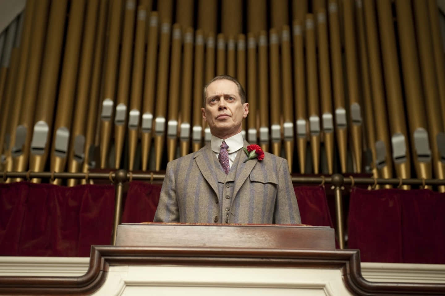 steve buscemi 桌布 壁紙 — 一名穿著條紋西裝的男子莊嚴地站在木製講壇前，身後是帶有紅色天鵝絨窗簾的大型管風琴。