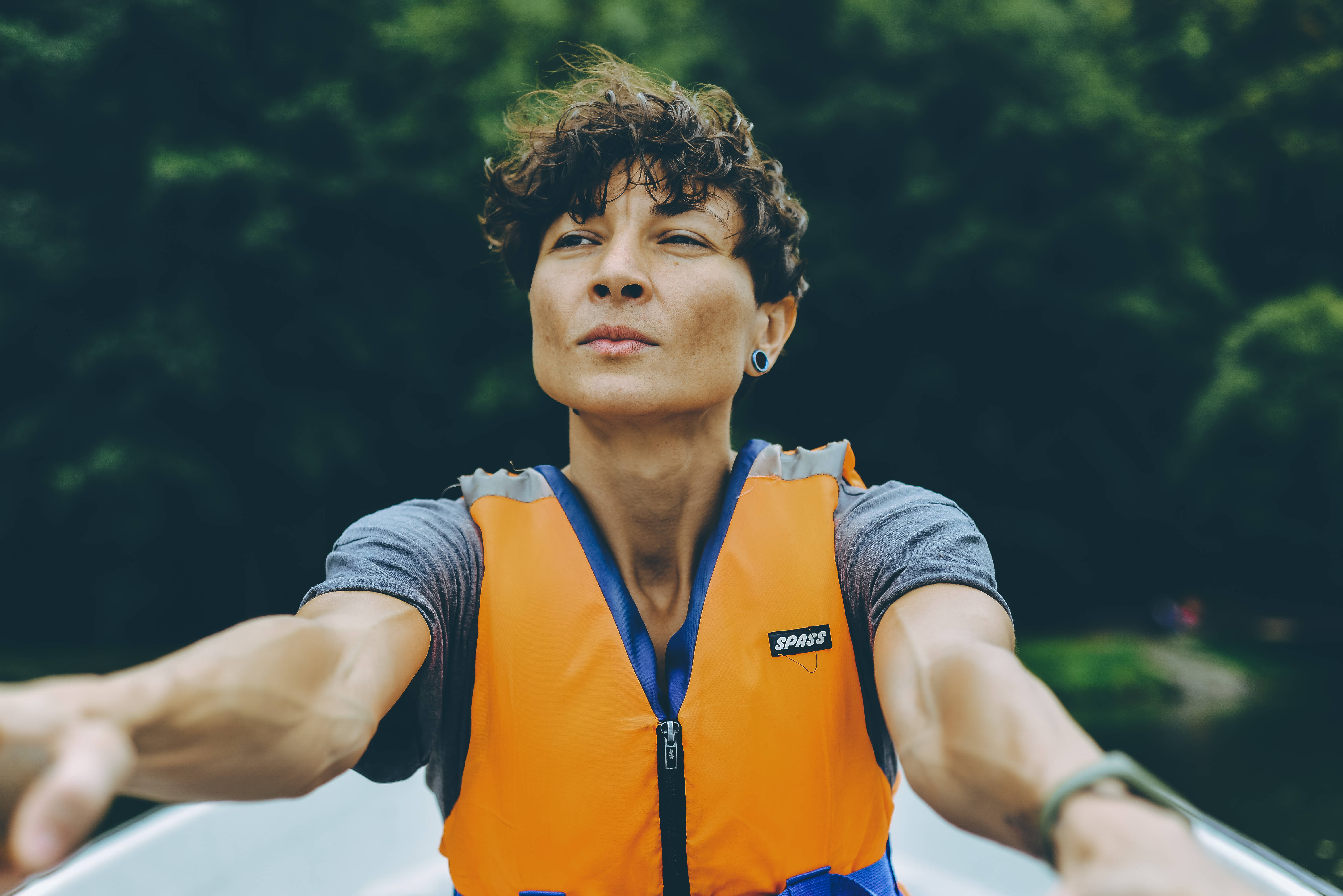 Tomboy 桌布 壁紙 — 一名穿著橙色救生衣的人在船上張開雙臂，周圍是茂密的綠色森林。