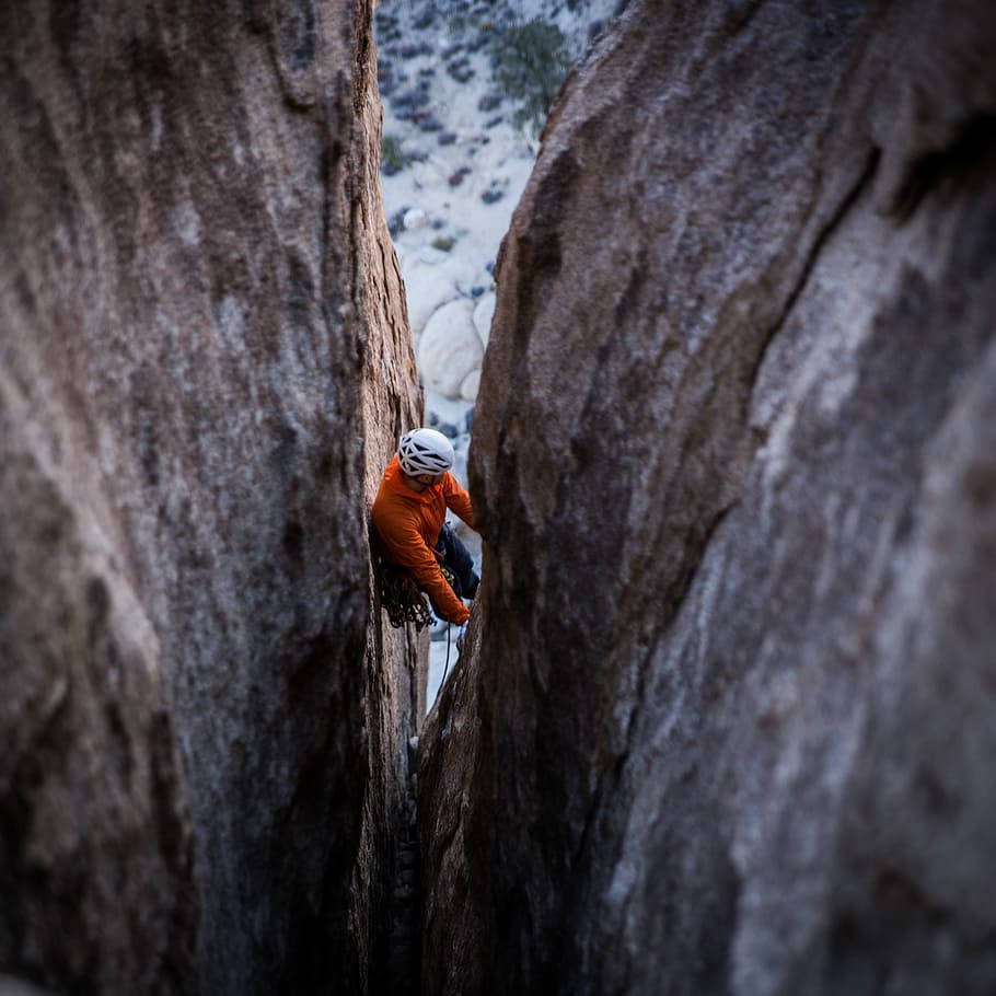 Climbing 桌布 壁紙 — 一名穿著橙色裝備的攀岩者，在柔和日光下，攀登著由高聳灰色巨石框住的狹窄岩石裂縫。
