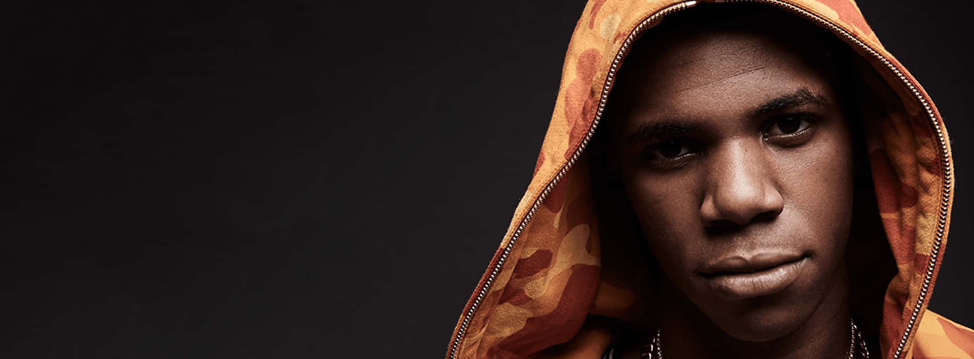 A Boogie Wit Da Hoodie 桌布 壁紙 — 一名穿著橙色迷彩連帽衫的年輕男子在深色背景下強烈凝視。