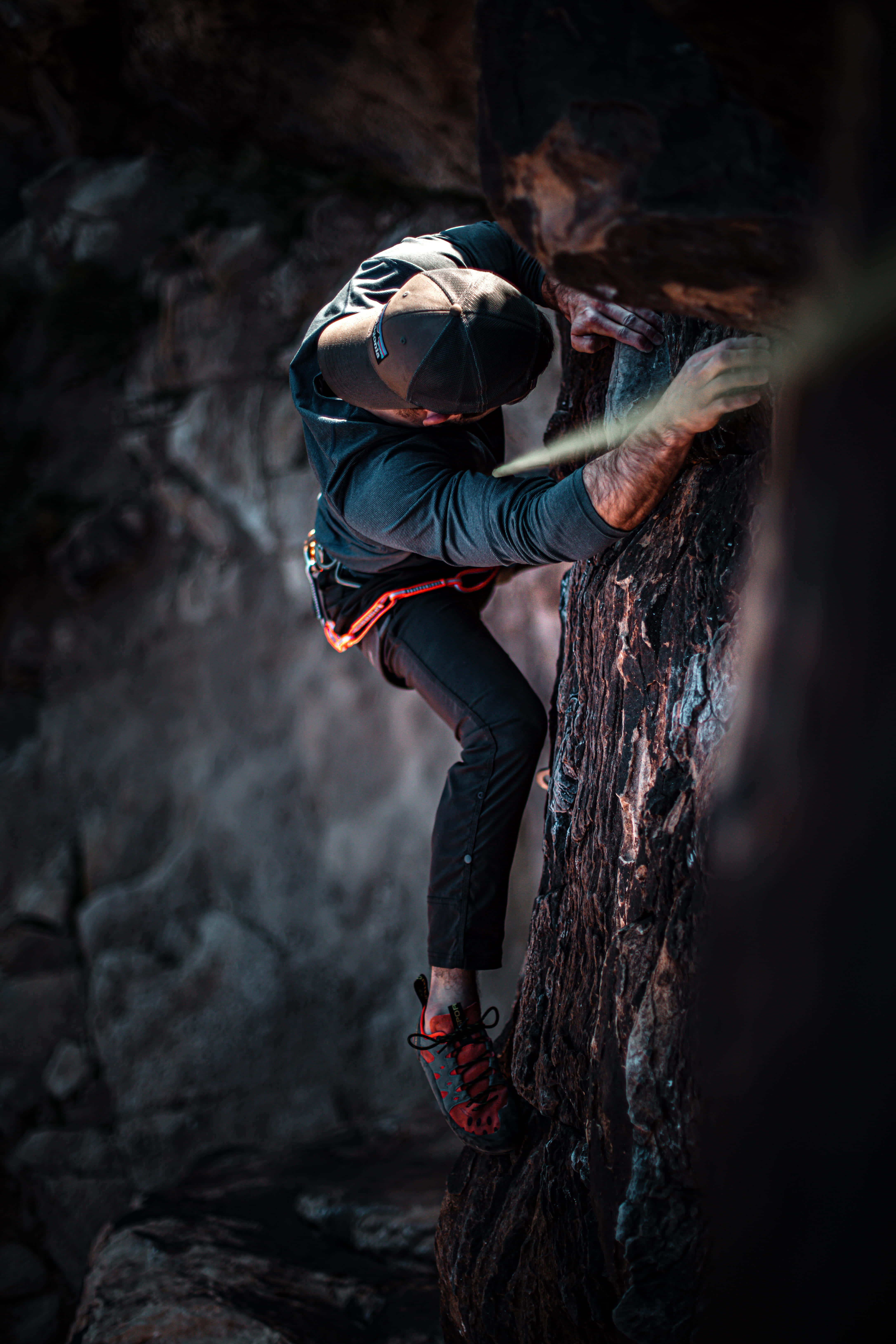 Climbing 桌布 壁紙 — 一名穿著深色裝備的攀岩者在戲劇性的燈光下，以高度專注力攀登崎嶇的岩壁。