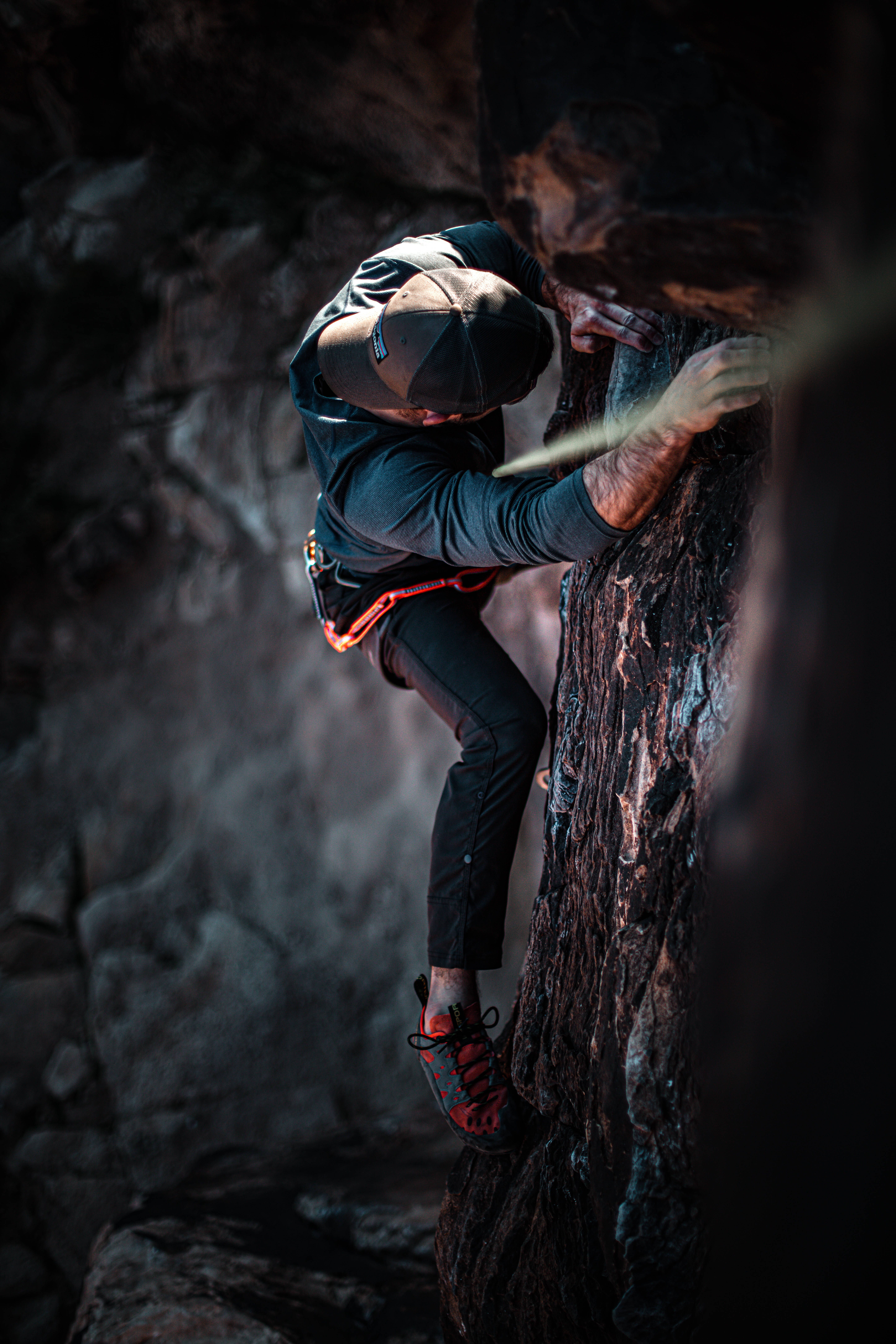 Rock Climbing 桌布 壁紙 — 一名穿著深色裝備的攀岩者在戲劇性燈光下，以高度專注力攀爬崎嶇的岩壁。