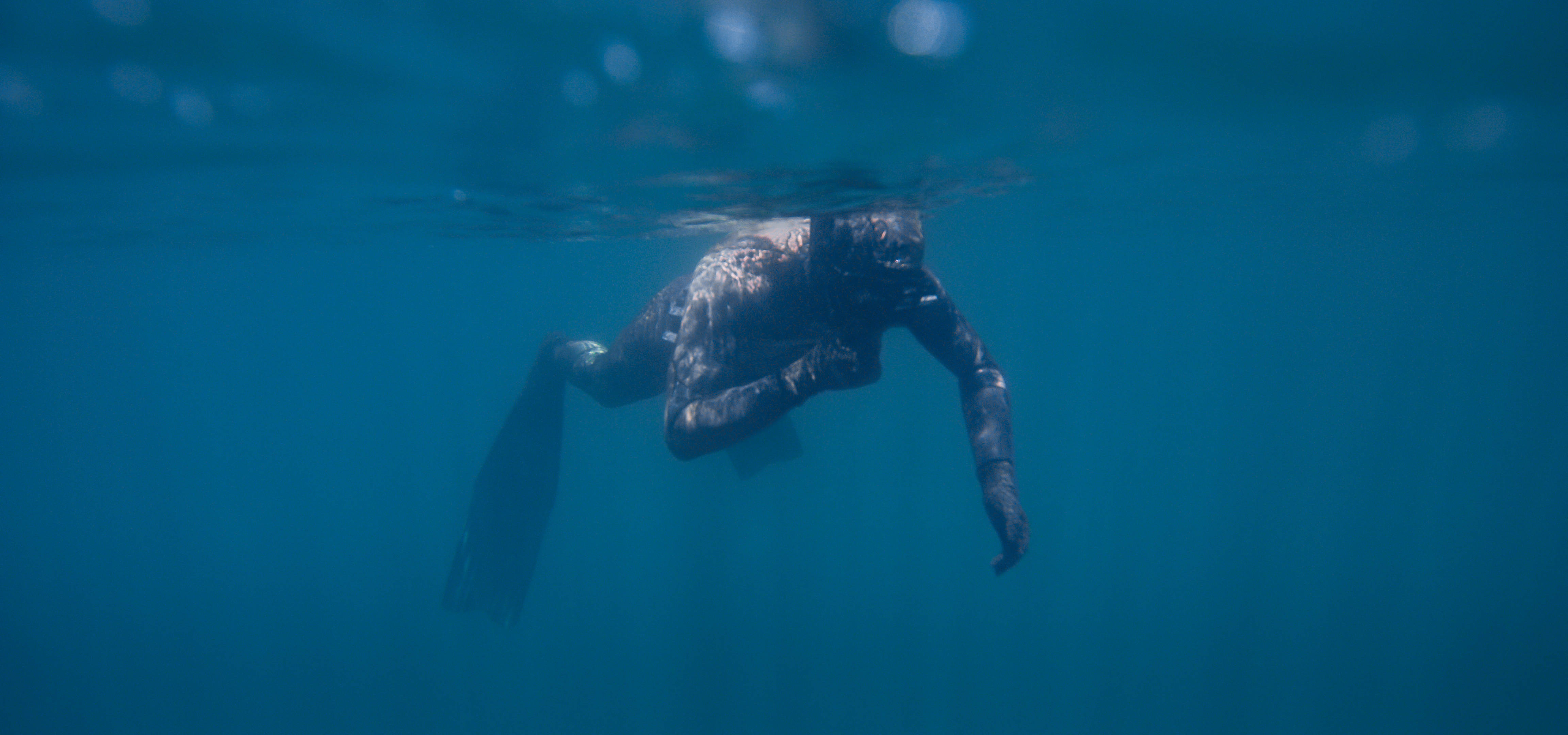Snorkeling 桌布 壁紙 — 一名穿著潛水衣的潛水員在清澈的藍色海水表面附近滑行，陽光穿透水面。