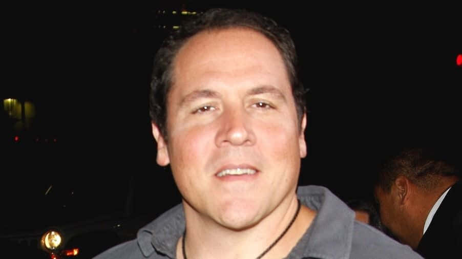 Jon Favreau 桌布 壁紙 — 一名穿著灰色襯衫的男子在夜間城市燈光下對著鏡頭微笑，背景人物模糊。