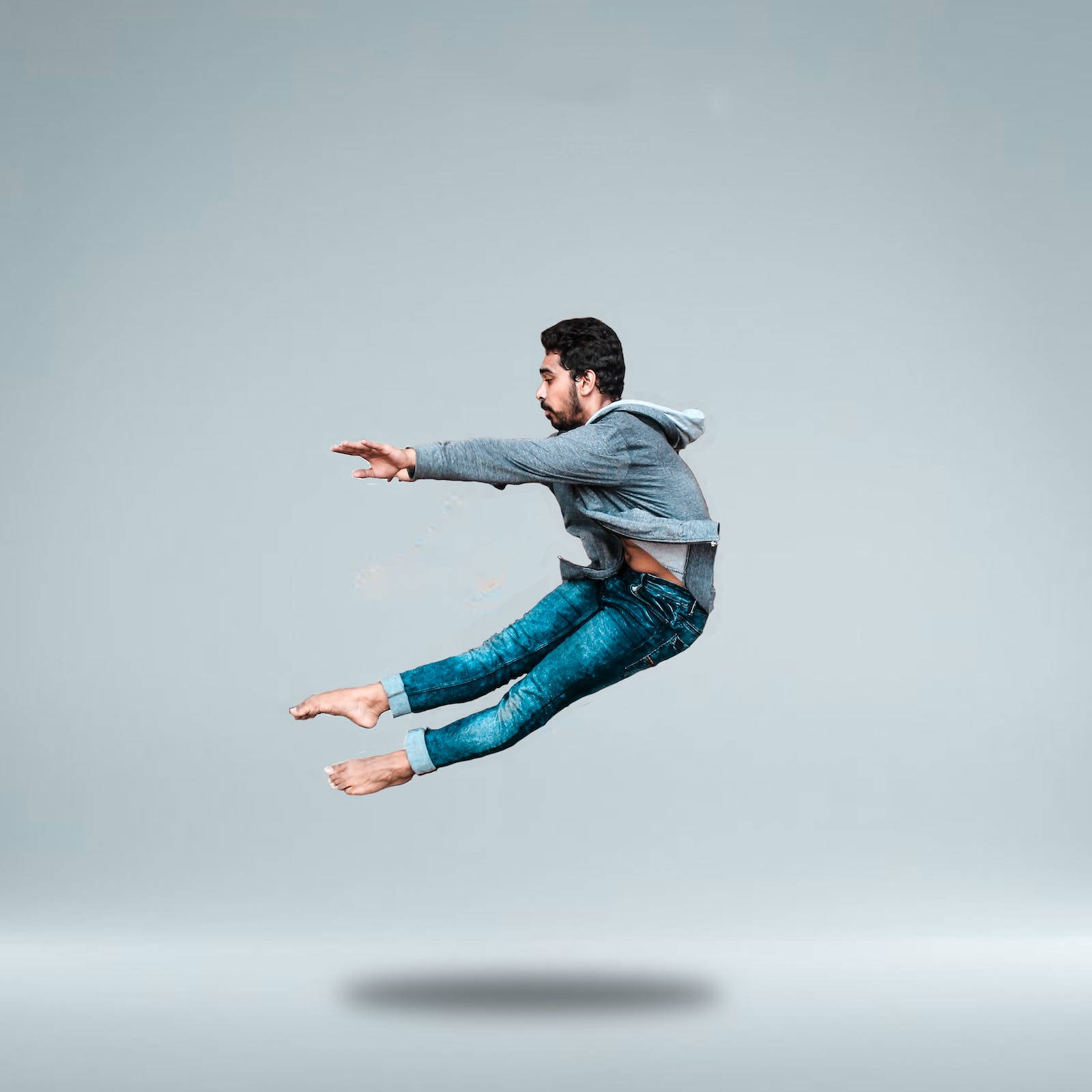 Jumping 桌布 壁紙 — 一名穿著牛仔褲和連帽衫的男子，在純灰色工作室背景前，下方有微妙的陰影，似乎懸浮在半空中。