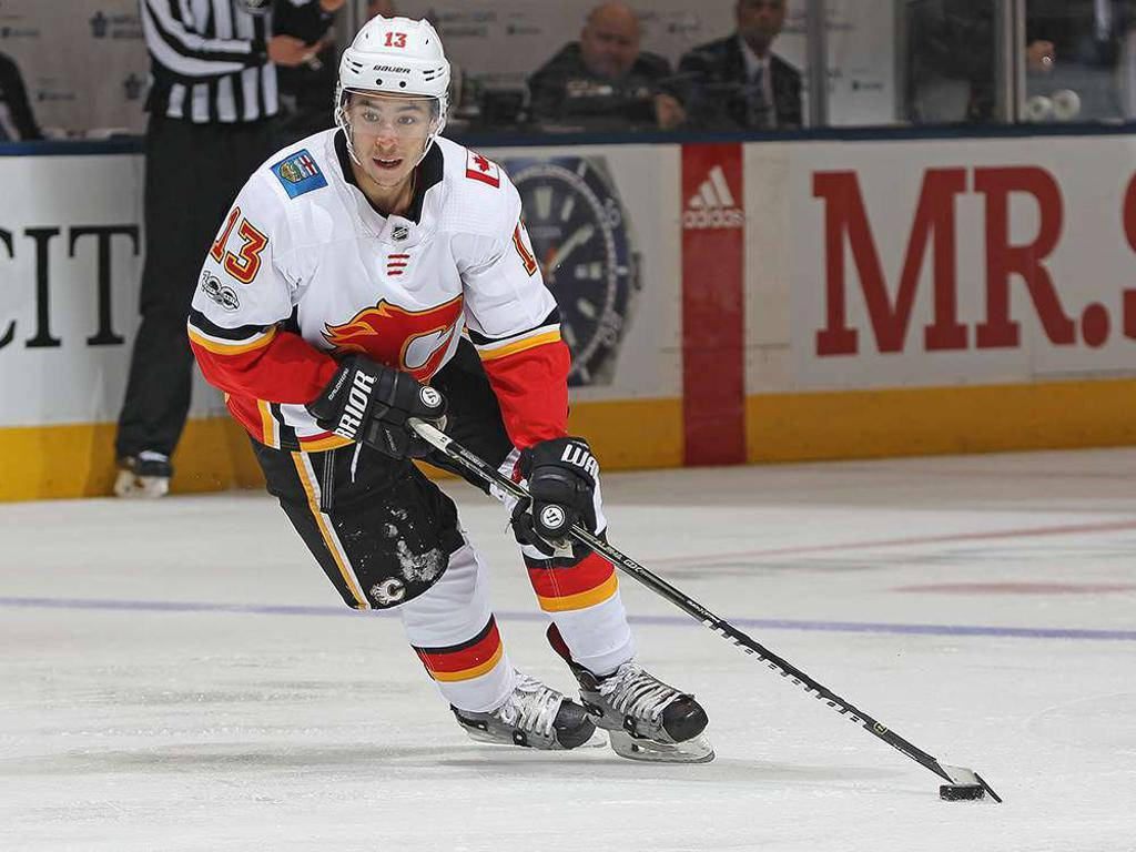 Johnny Gaudreau 桌布 壁紙 — 一名穿著白色、紅色和黑色球衣的冰球運動員在比賽中拿著球桿在冰上激烈滑行。
