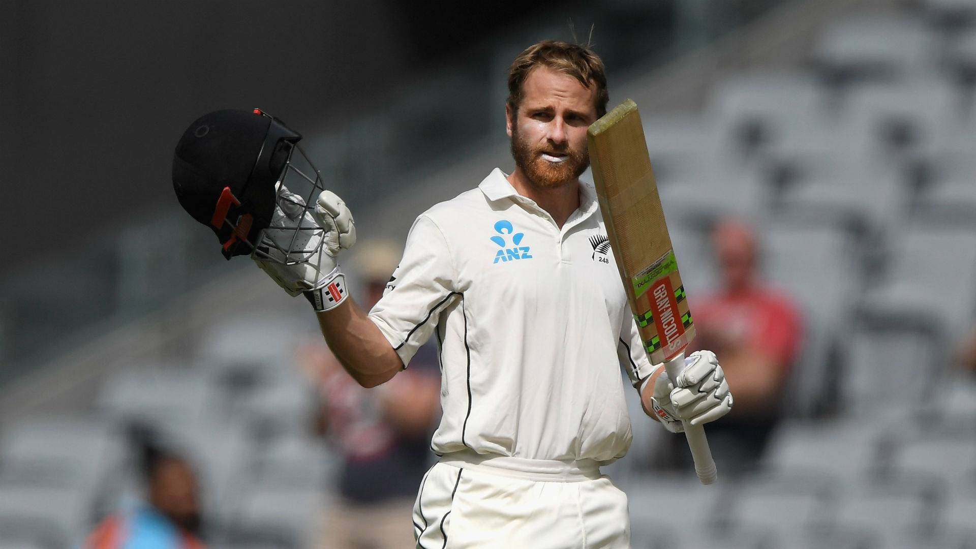 kane williamson 桌布 壁紙 — 一名穿著白色制服的板球運動員在明亮的日光下走在體育場上，手持球棒和頭盔。