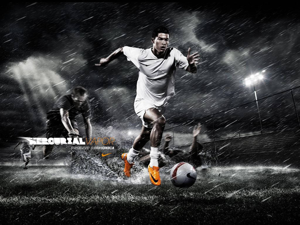 Ronaldo 桌布 壁紙 — 一名穿著白色和橙色球靴的足球員在夜間球場燈光下於大雨中盤球。