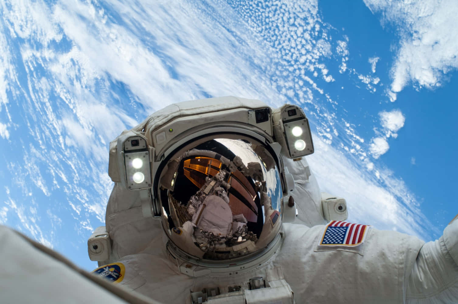 NASA 動態圖片 桌布 壁紙 — 一名穿著白色太空衣的太空人，戴著反光頭盔，漂浮在地球藍白雲層的背景前。