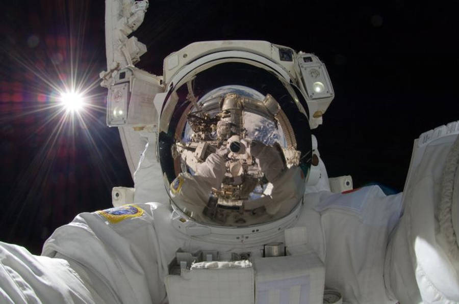 Astronaut In Space 桌布 壁紙 — 一名穿著白色太空衣的太空人在國際太空站外漂浮，太陽在他身後對著太空的黑色虛空燃燒。