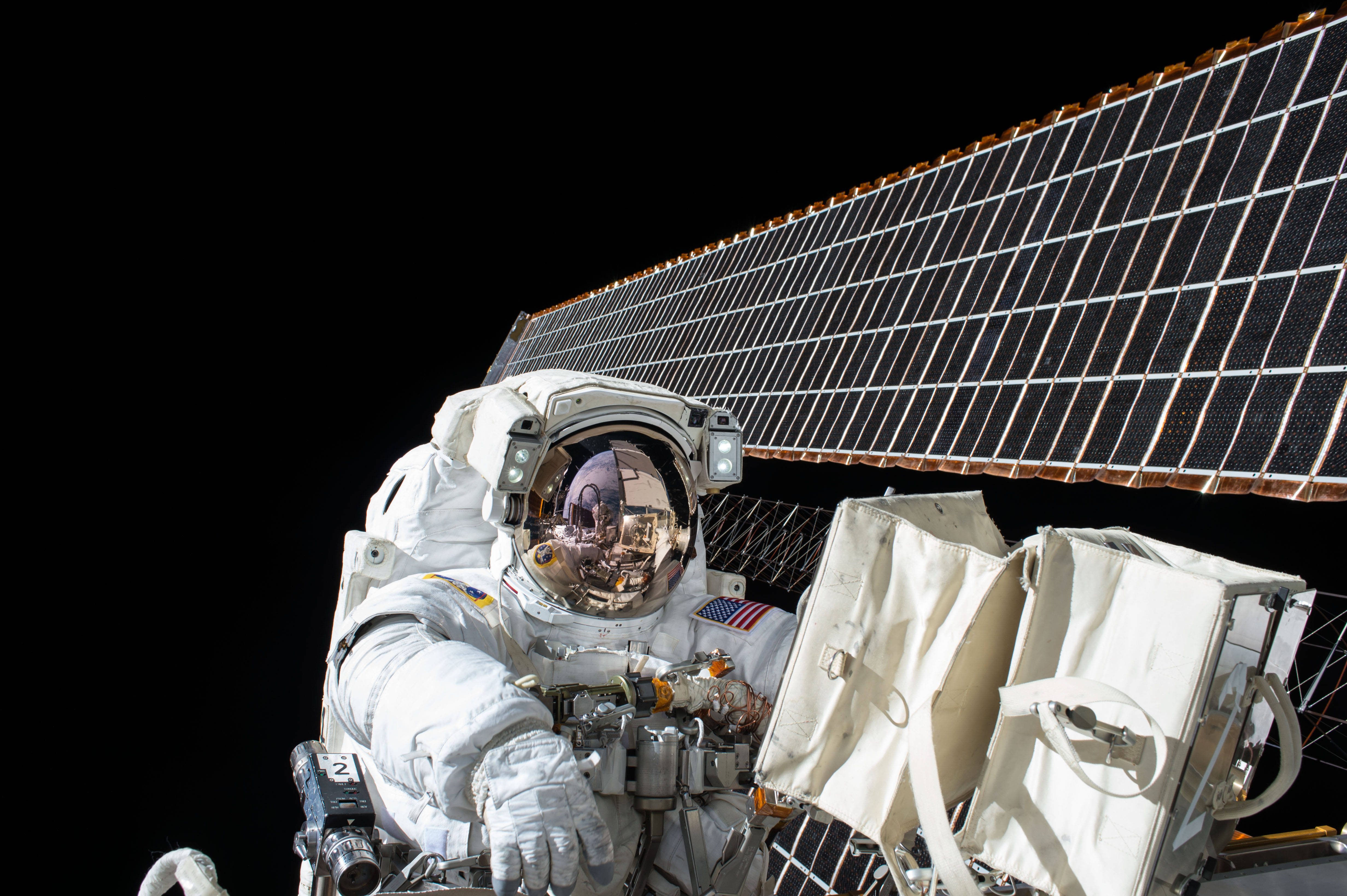 NASA 動態圖片 桌布 壁紙 — 一名穿著白色太空衣的太空人在太空船外進行太空漫步，背景是太空的黑色虛空和太陽能板。