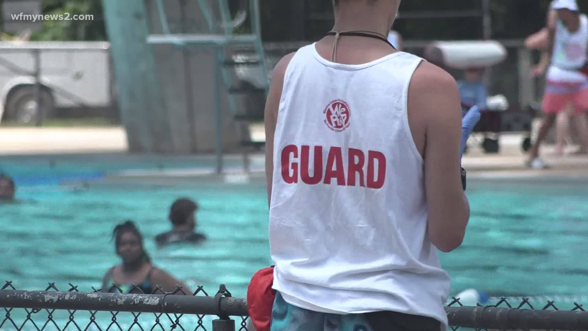 Vacation 桌布 壁紙 — 一名穿著白色背心、上面有紅色「GUARD」字樣的救生員，站在有圍欄的游泳池旁，在陽光明媚的日子裡觀察游泳者。