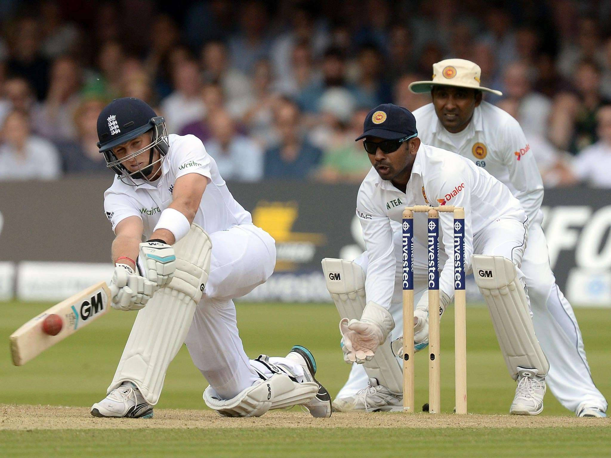 England Cricket 桌布 壁紙 — 一名穿著白色裝備的板球擊球手揮棒擊打紅色球，而守門員和投球手在綠色場地上專注地觀看。