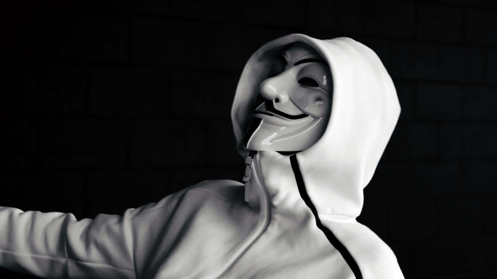 Mask 桌布 壁紙 — 一名穿著白色連帽衫的人，在戲劇性燈光下，戴著蓋伊·福克斯面具，背景是深色磚牆。