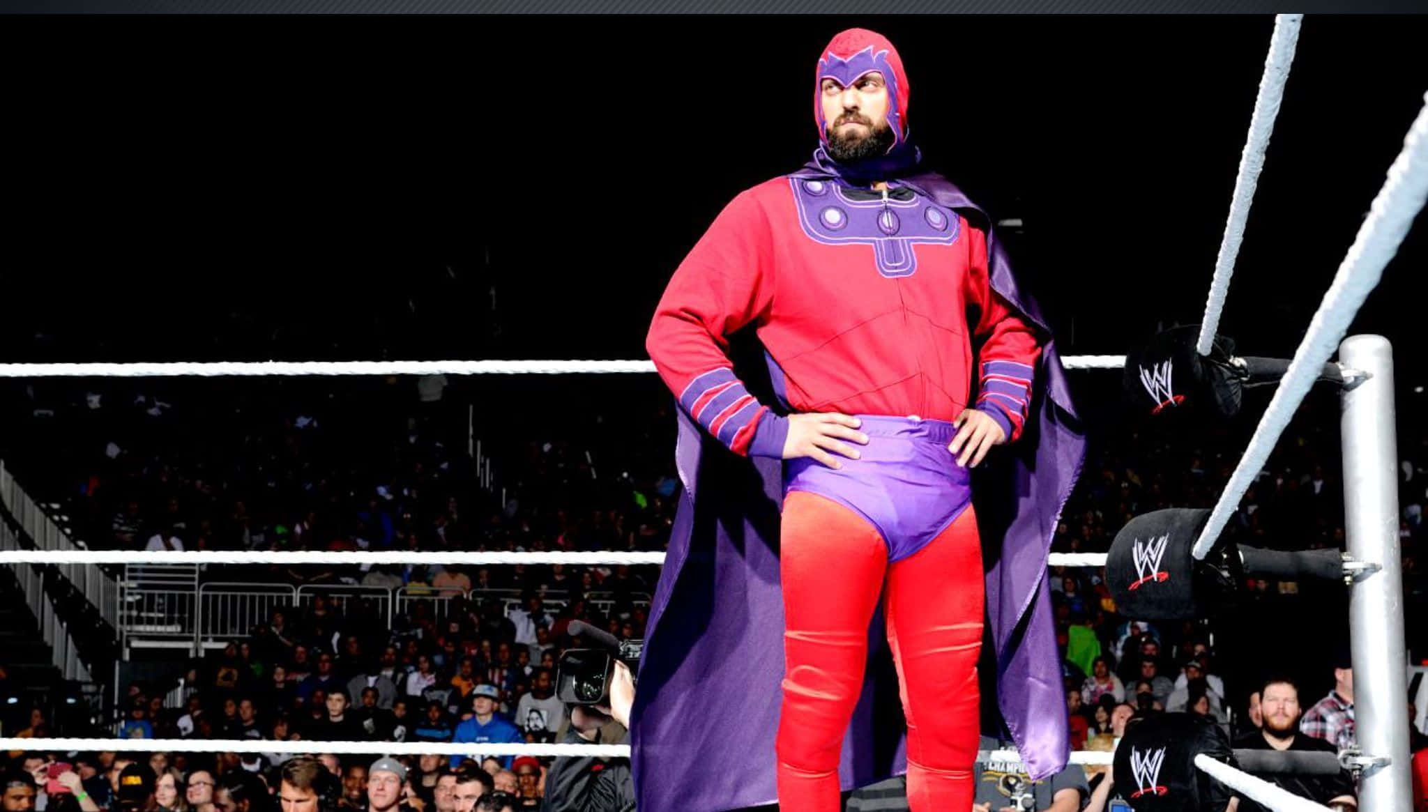 WWE 桌布 壁紙 — 一名穿著紅紫色超級英雄服裝的摔角手自信地站在摔角場上，身後有歡呼的人群。