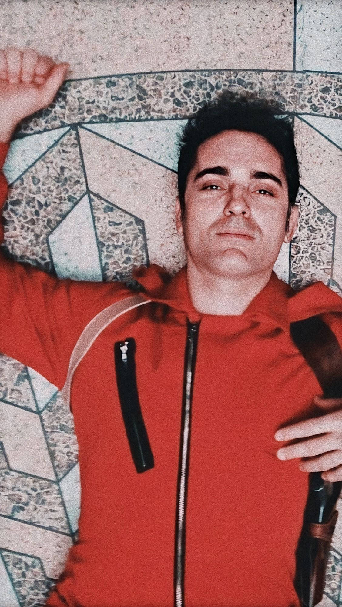 Berlin Money Heist 桌布 壁紙 — 一名穿著紅色拉鍊連帽衫的男子躺在幾何水磨石地板上，雙臂伸展，表情平靜。