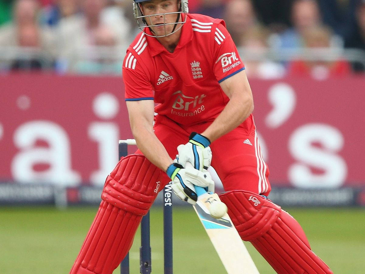 jos buttler 桌布 壁紙 — 一名穿著紅色裝備的板球選手在擊球區蹲下，握緊球棒準備擊球。